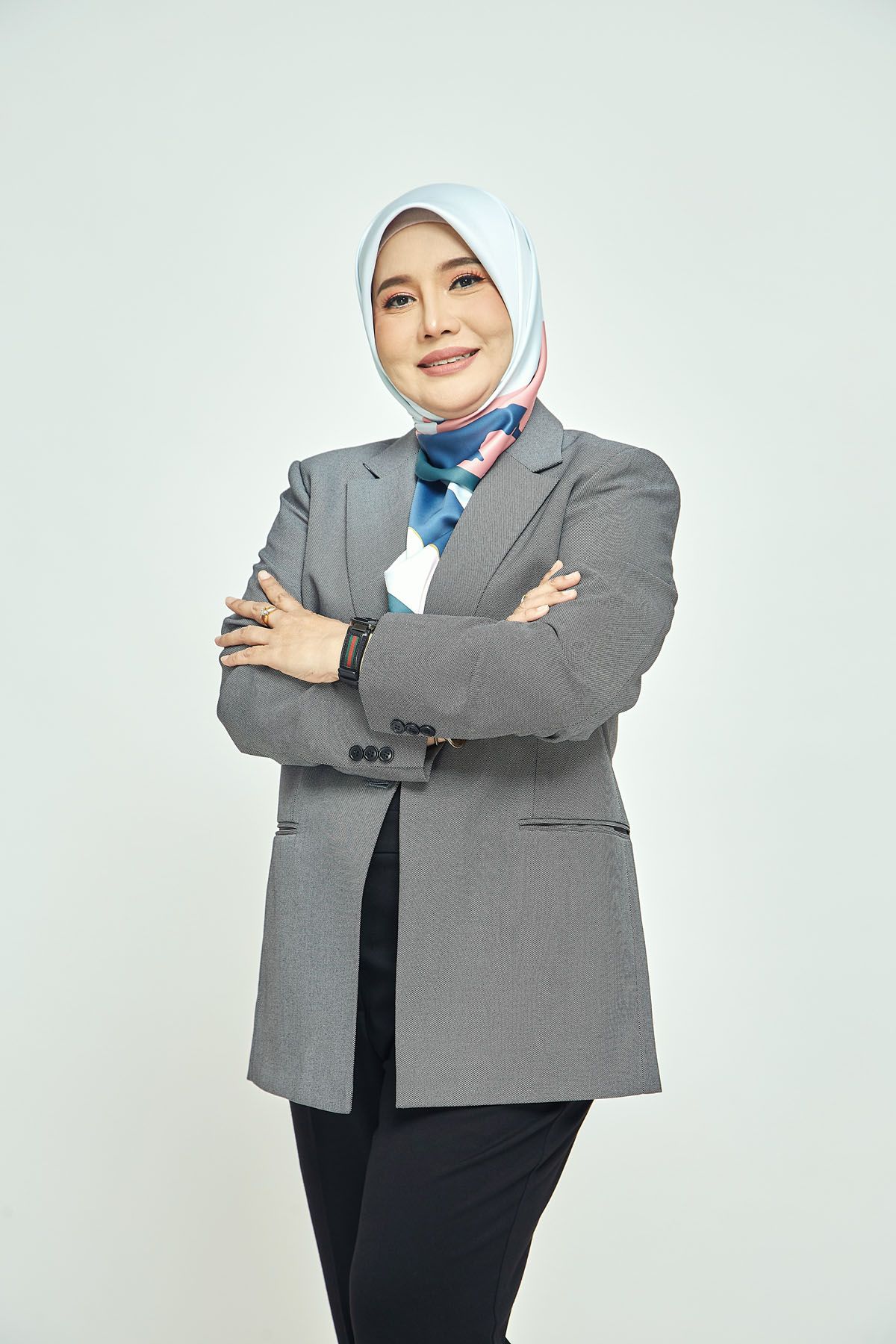 Professional Muslim woman in grey blazer and blue hijab standing with arms crossed confidently.