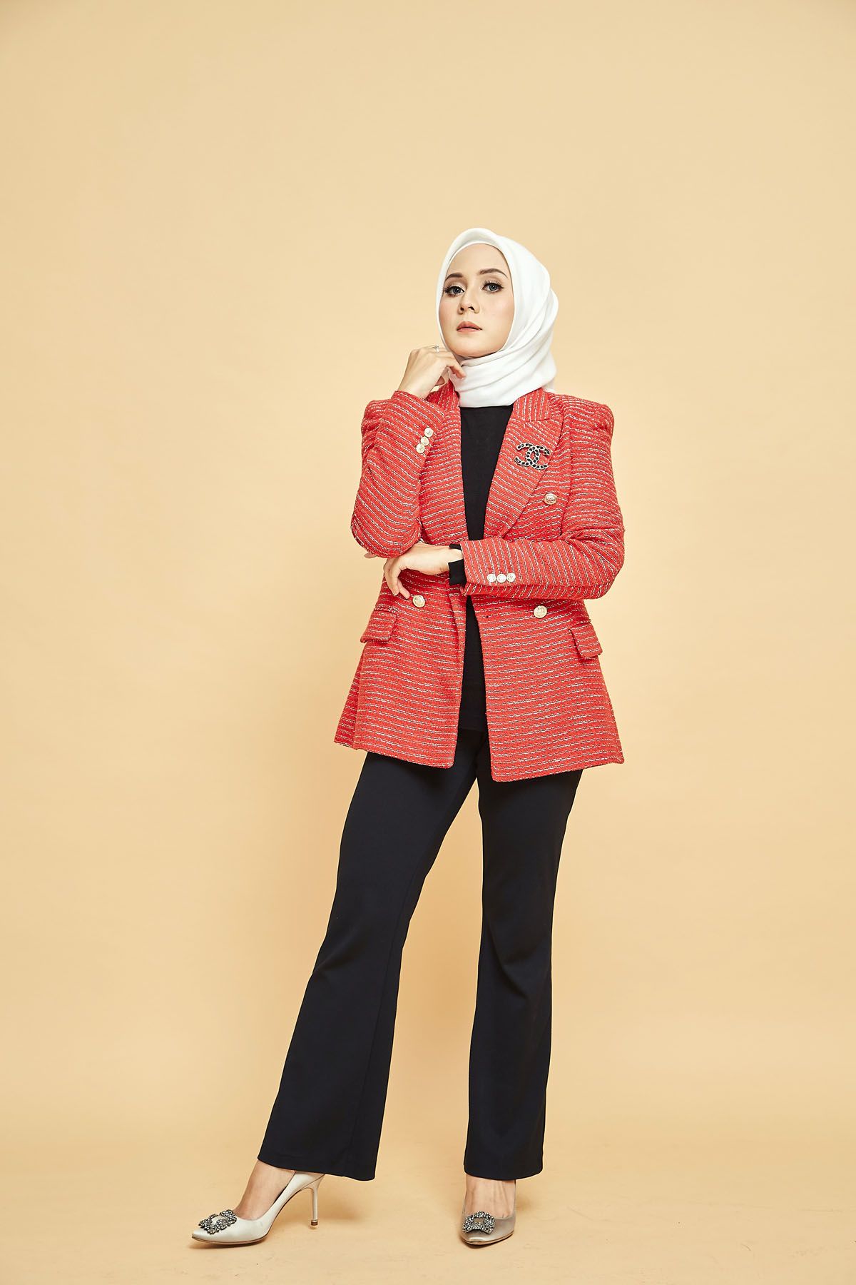 Muslim woman in white hijab and red tweed blazer with black pants posing on beige background.