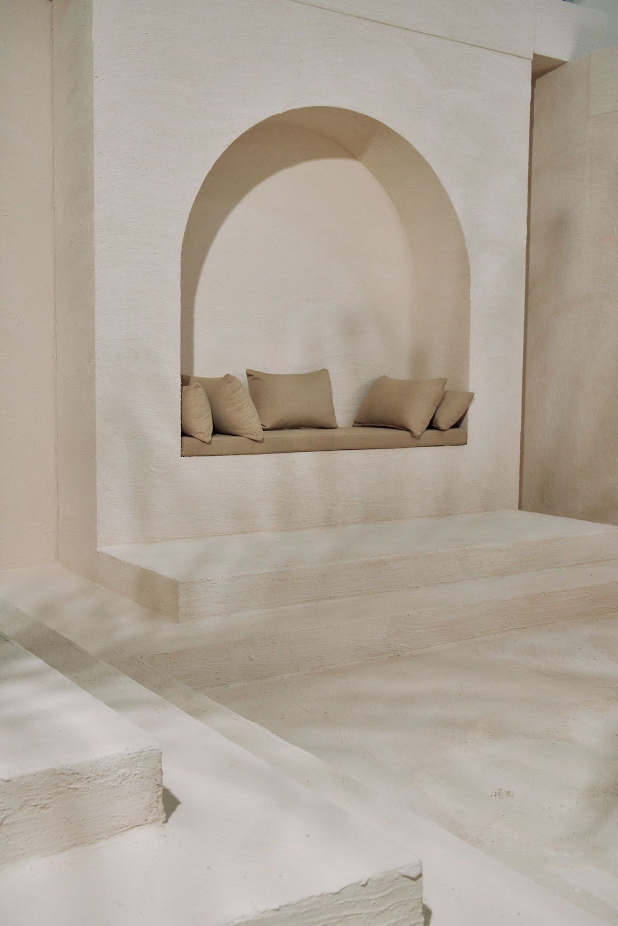 Minimalist white plaster interior featuring an arched niche with neutral linen cushions on built-in bench.