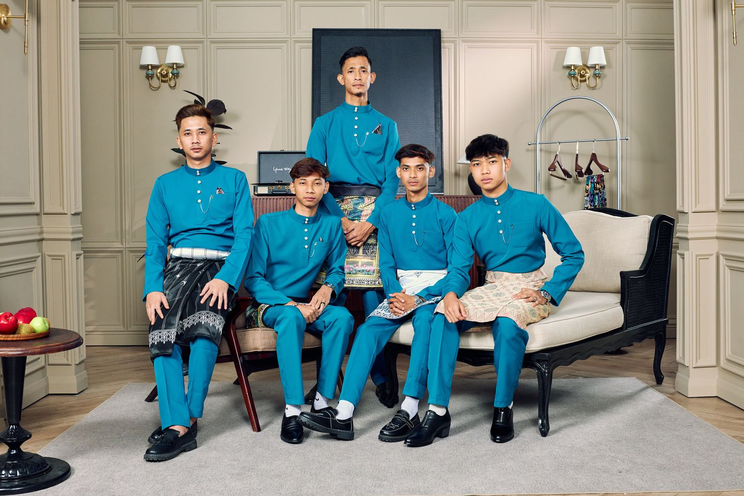 Five young men in matching teal Baju Melayu traditional Malaysian outfits posing together on a sofa.