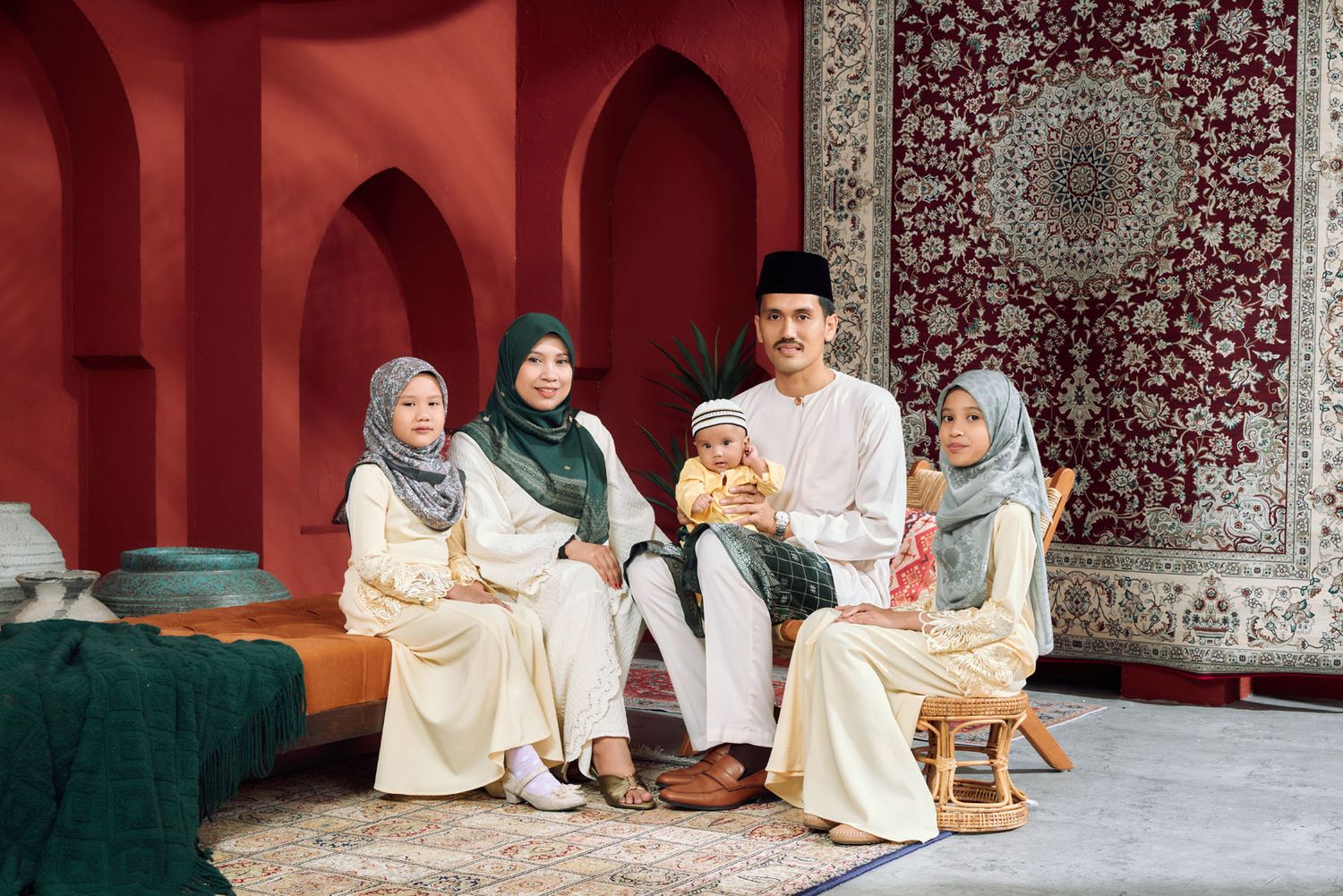 Muslim family in traditional Baju Kurung and Baju Melayu attire posed together in a red arched setting.