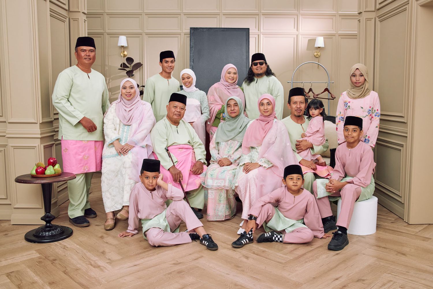 Large Malaysian family group portrait in coordinating pink and mint green traditional Eid outfits indoors.