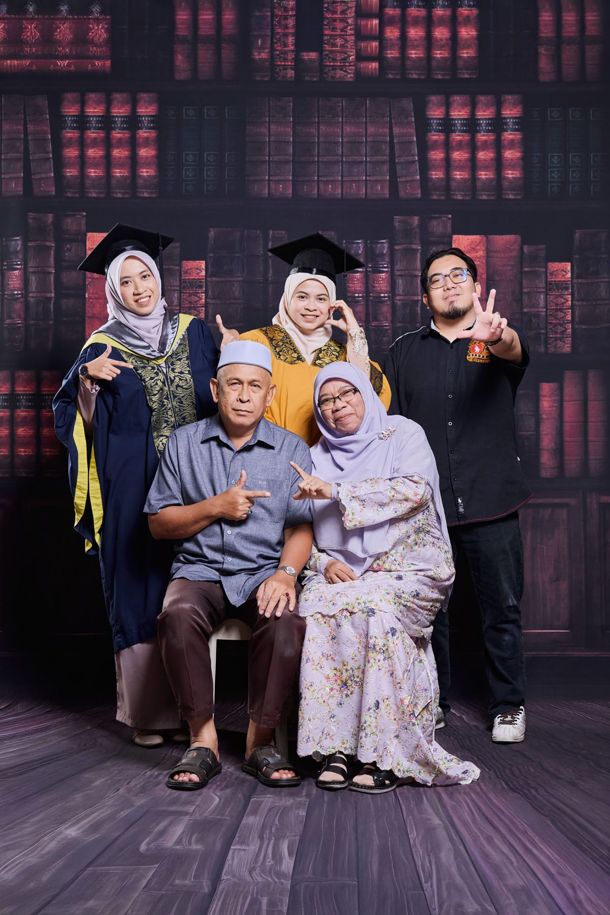 Happy Muslim family graduation portrait with two graduates in caps and gowns with parents.