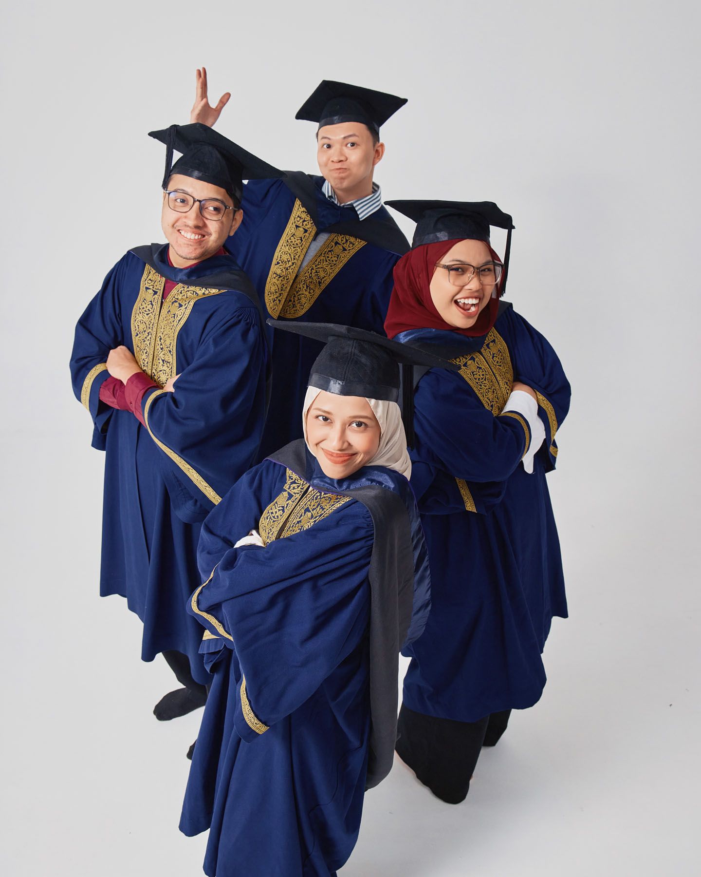 Four graduates in navy mortarboards making fun poses for graduation pictures.