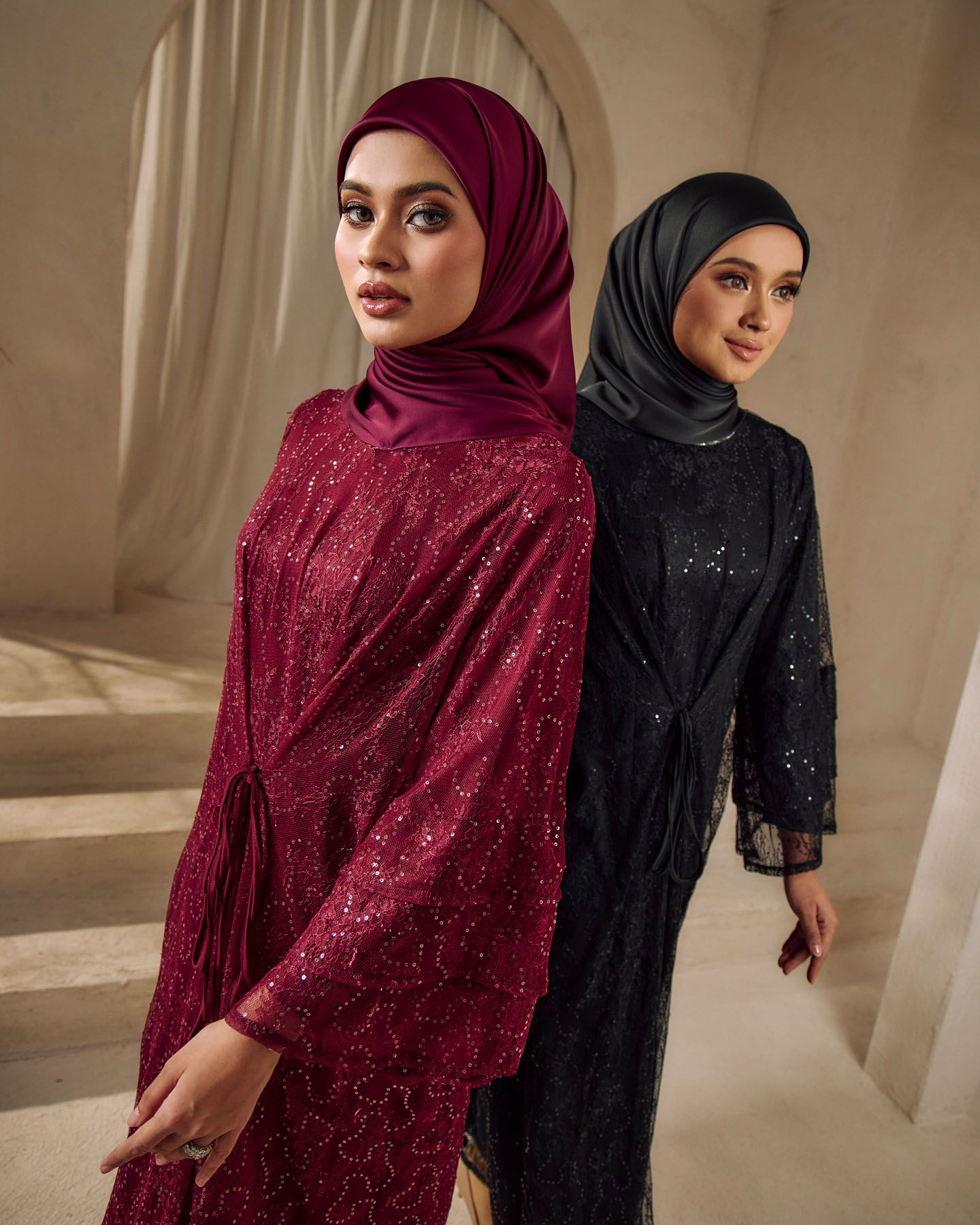 Two women in sparkly burgundy and black hijab abayas pose together.