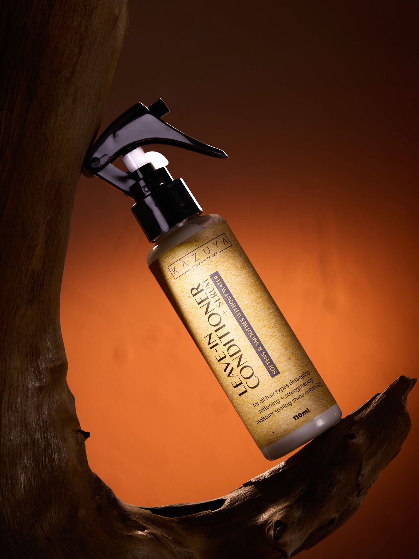 KAZUYA Leave-In Conditioner spray bottle displayed upside down against warm orange background with driftwood prop.