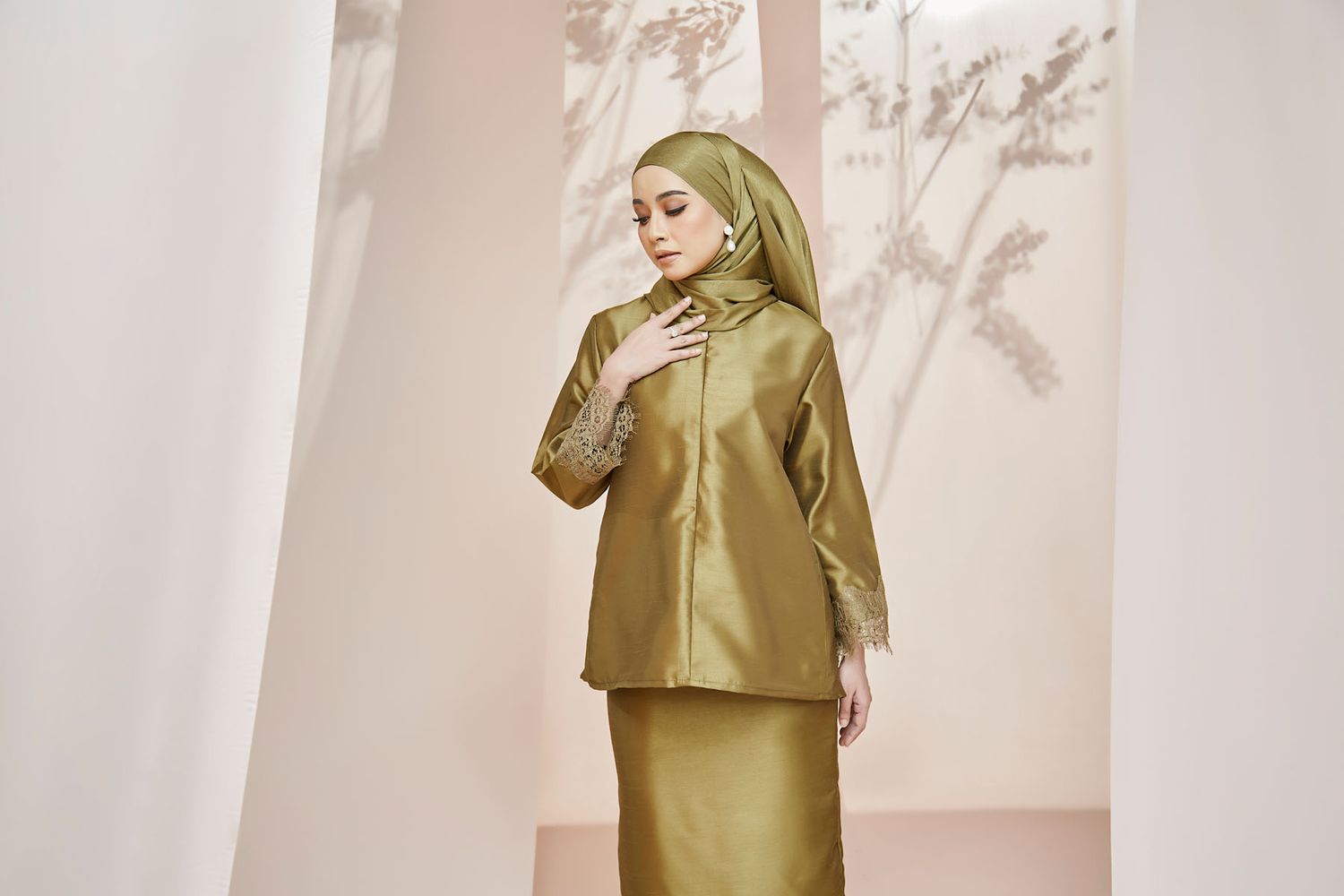 Woman wearing olive green satin baju kurung with lace detail sleeves and matching hijab.