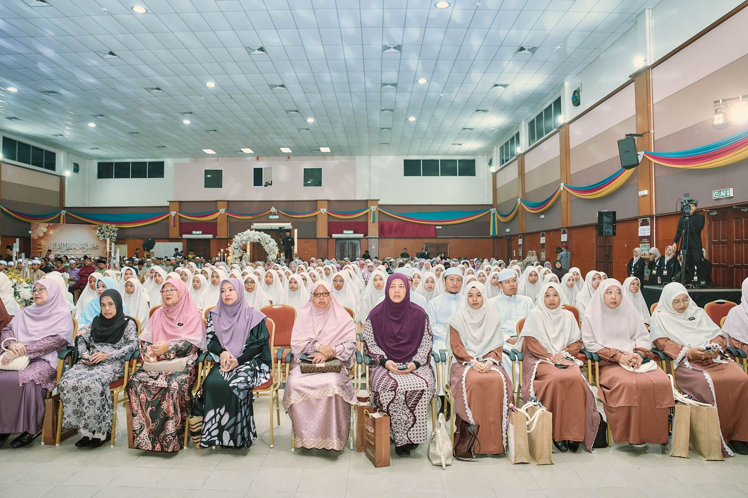 Large group of Muslim women in colorful hijabs seated together at a formal Islamic ceremony in Malaysia.