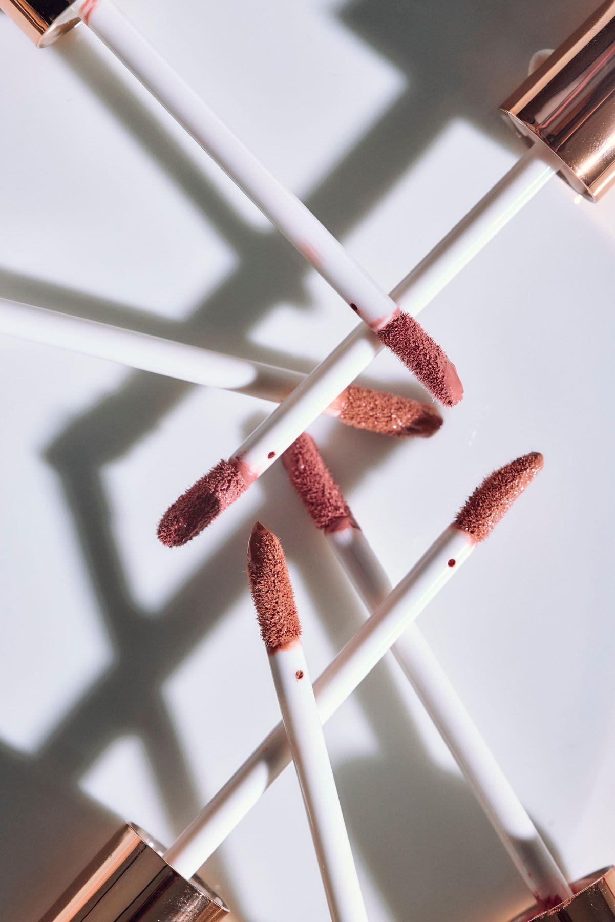 Multiple lip gloss applicators with mauve glitter wands arranged in a geometric pattern on white background.