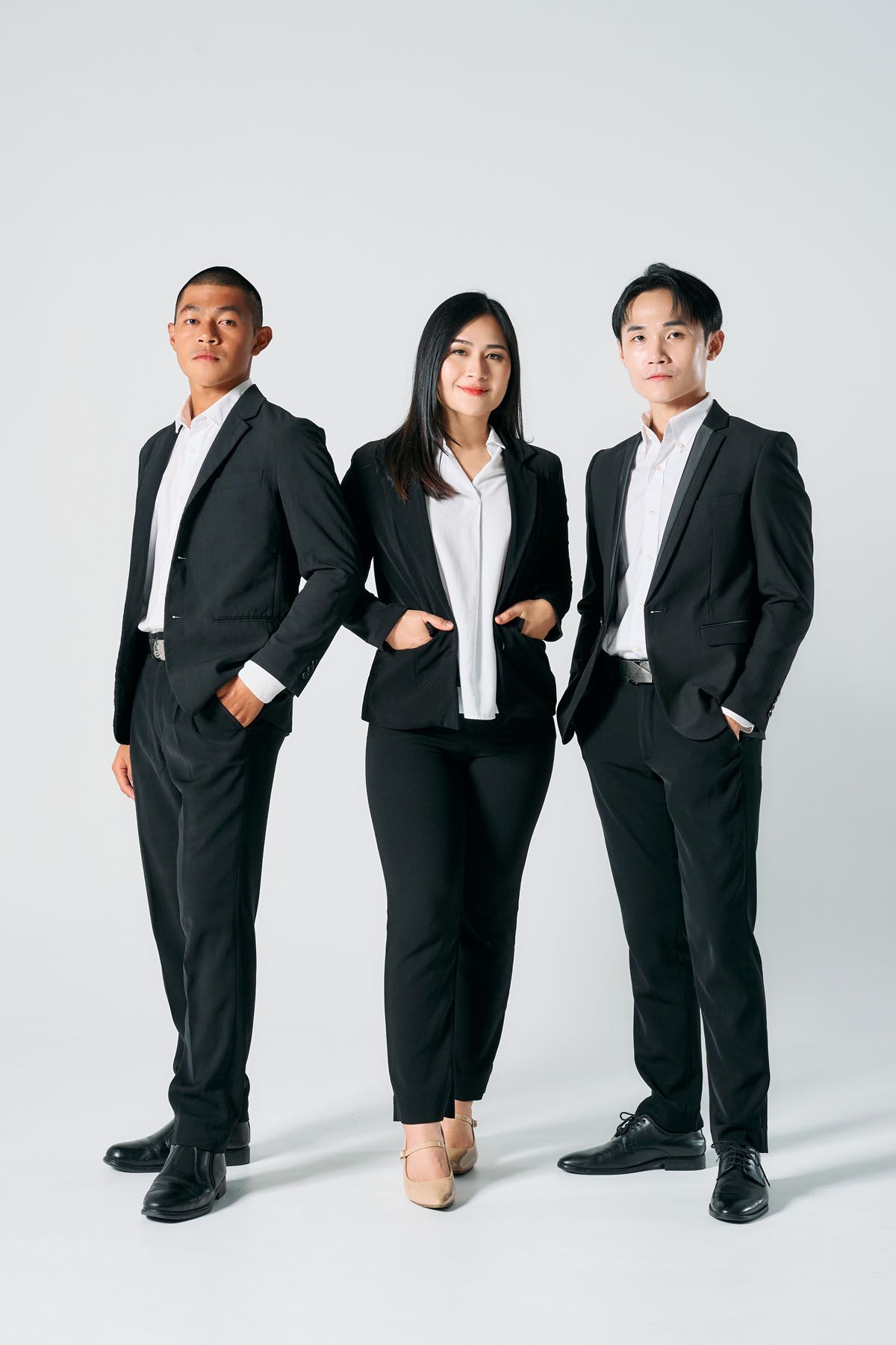 Three young Asian business professionals in black suits pose confidently against a white background.