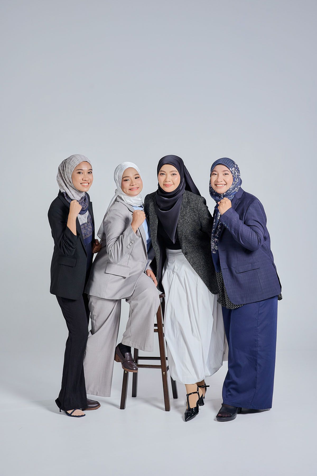 Four Muslim women in hijabs and professional attire posing confidently together in a studio setting.