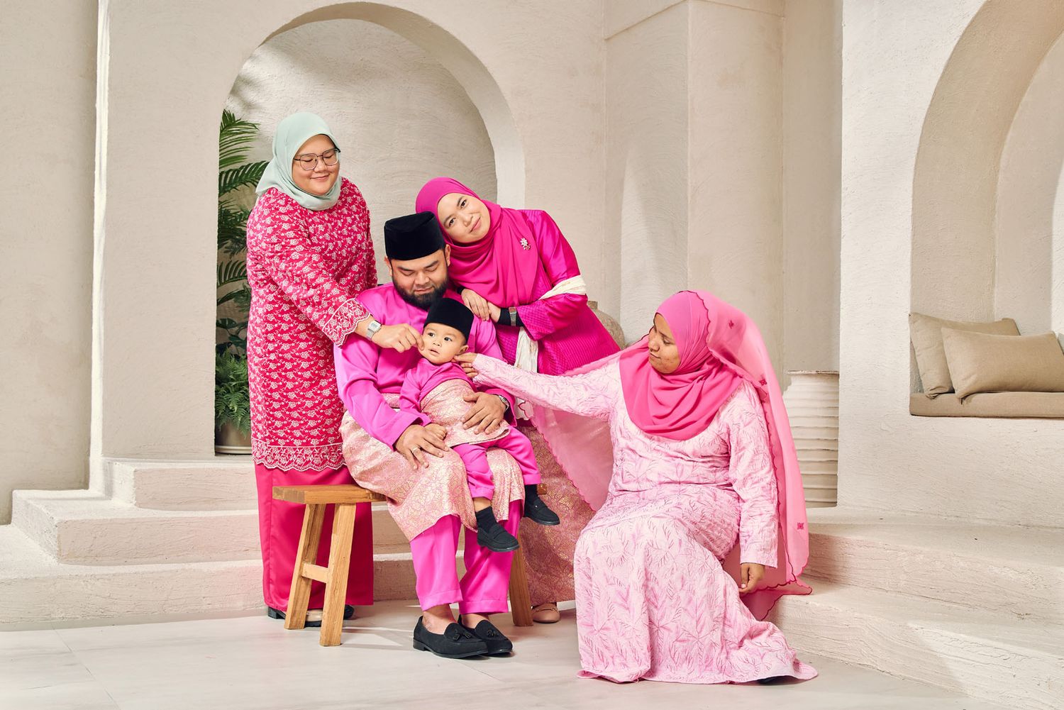 Multi-generational Malaysian family in vibrant pink traditional attire posing for festive Eid portrait.