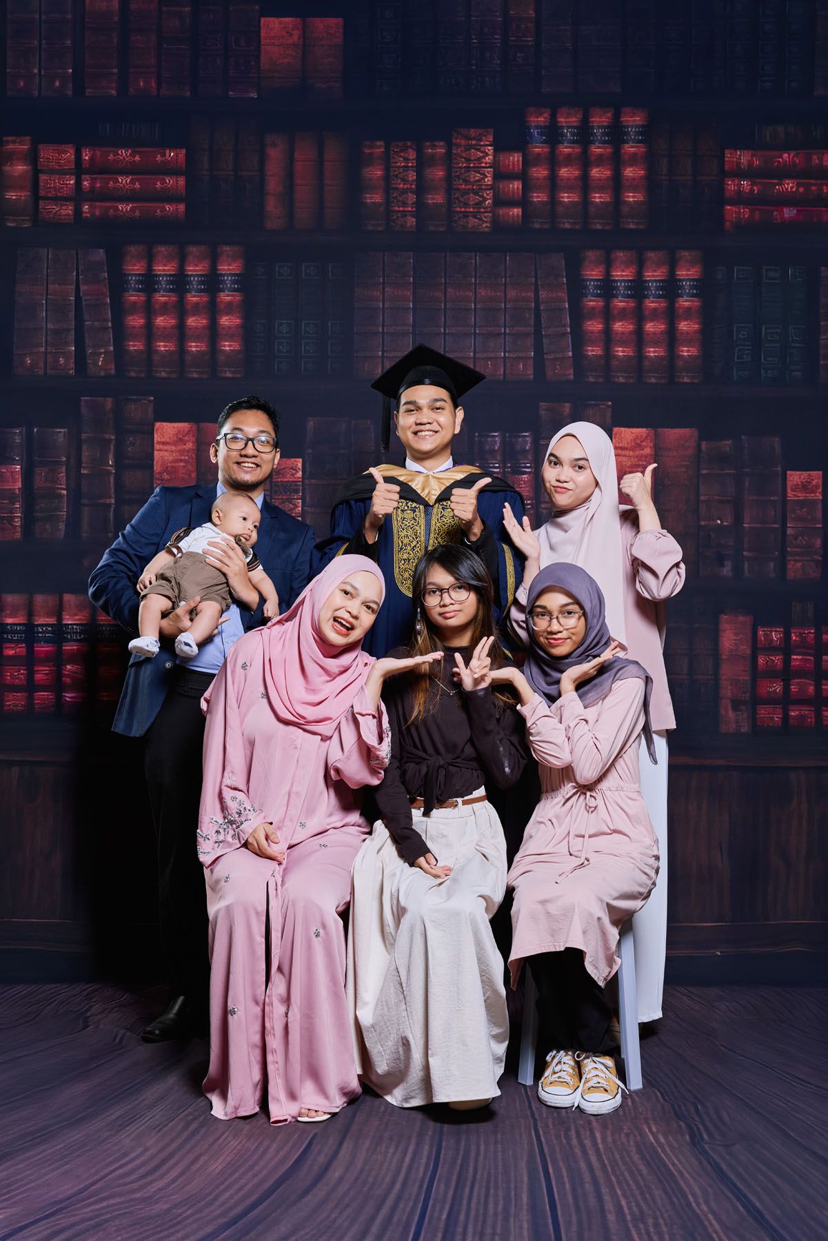 Group of siblings celebrating graduation with young man in blue convocation robe and mortarboard cap.