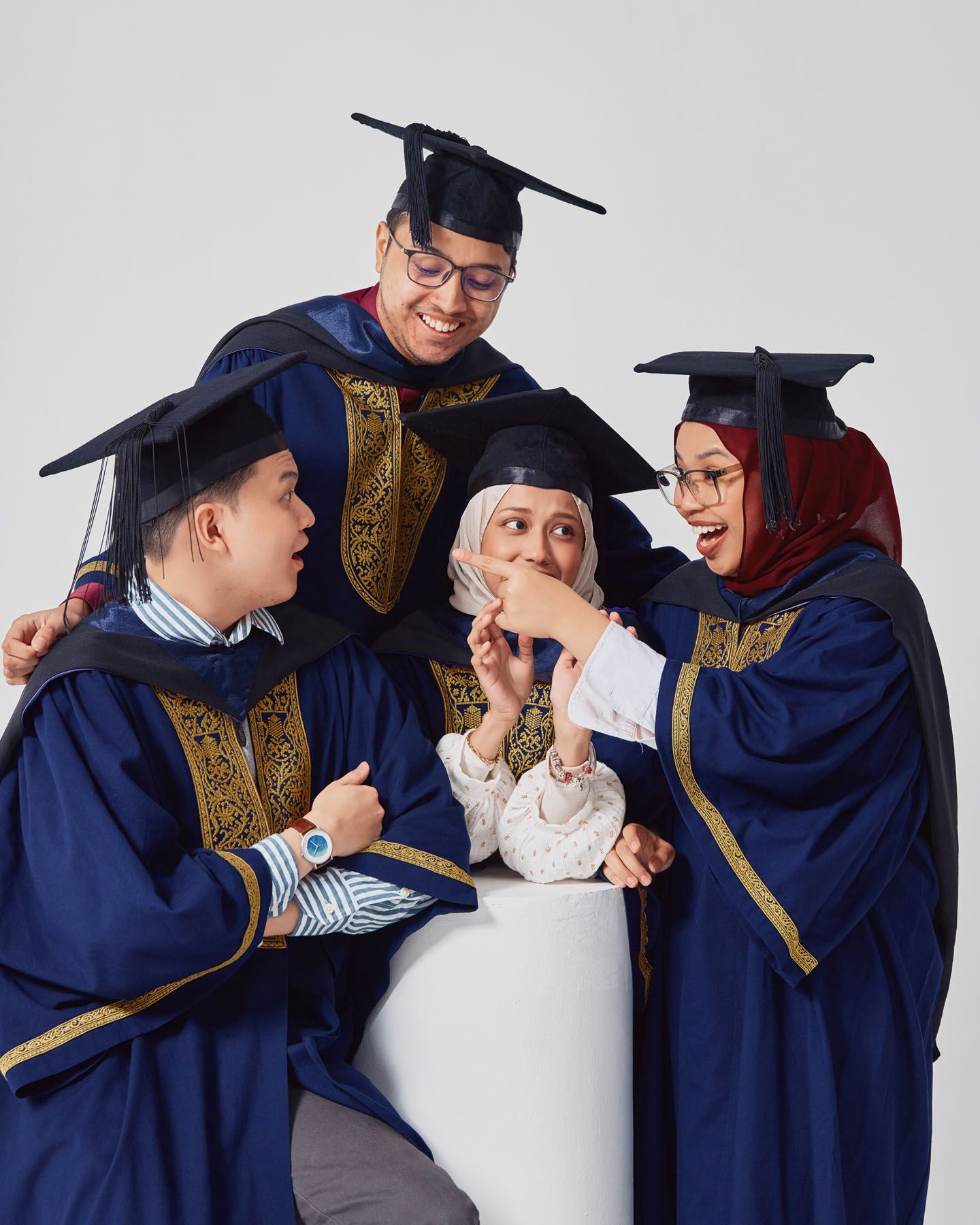 Four graduates in navy robes laughing together during graduation photo session.
