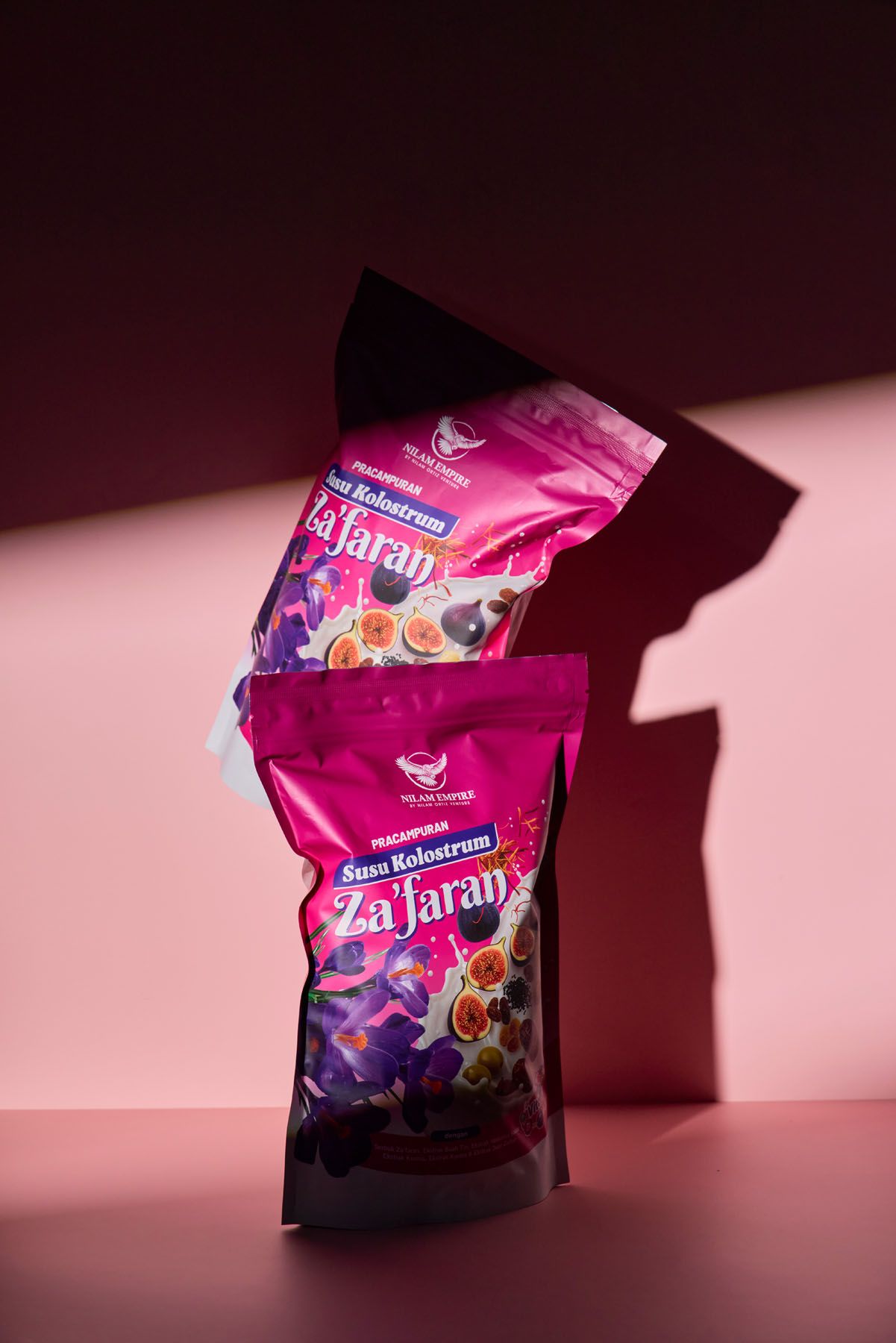 Pink Za'faran Susu Kolostrum supplement powder packets stacked dramatically against a dark pink background.