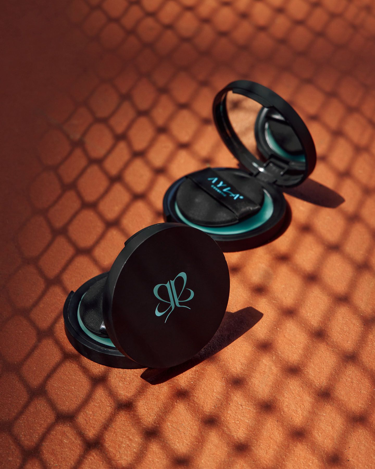 Open black AZA cosmetic compact with teal mirror detail casting dramatic shadows on terracotta background.