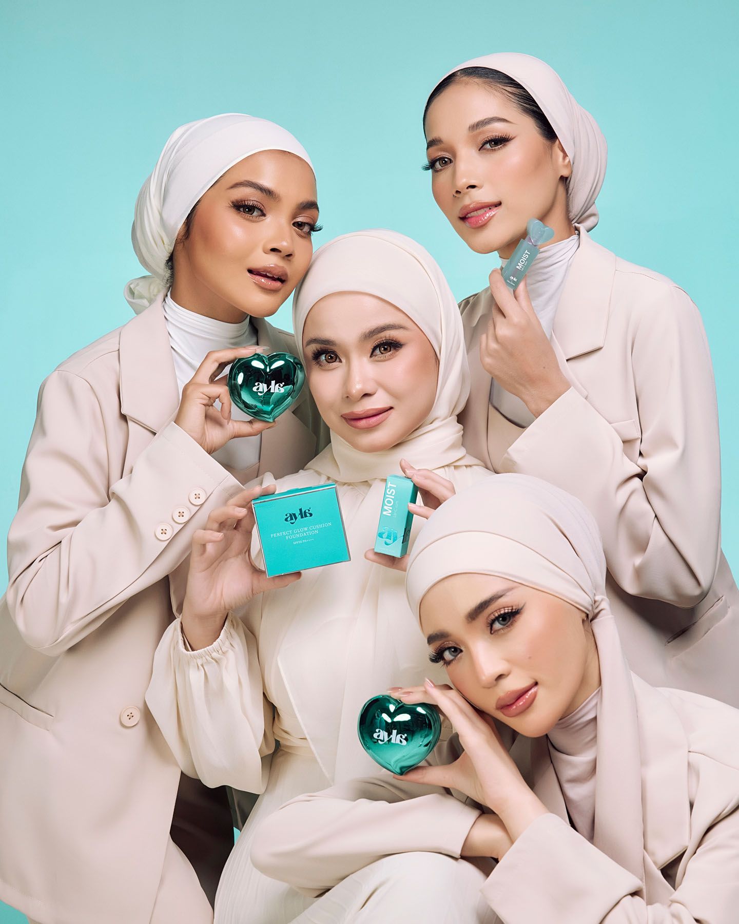 Four women in beige hijabs pose together holding teal heart-shaped beauty products.