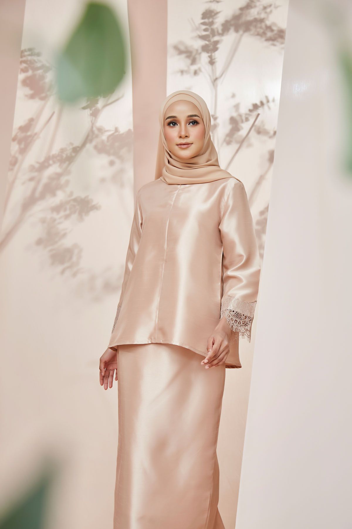 Woman in champagne gold satin baju kurung with lace cuffs and matching hijab in elegant pose.