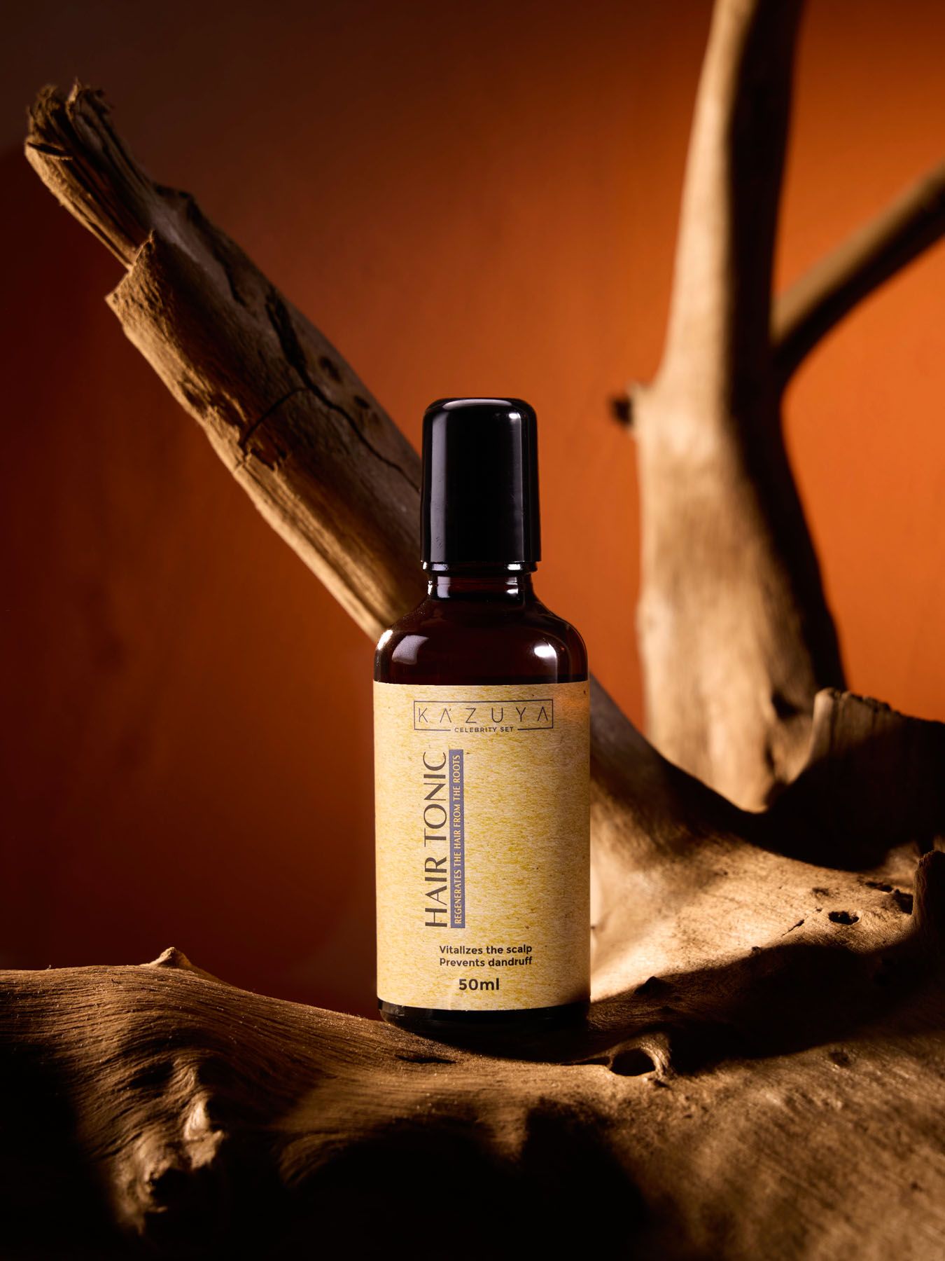 KAZUYA Hair Tonic 60ml amber bottle for scalp moisture and hair growth displayed on rustic driftwood orange backdrop.