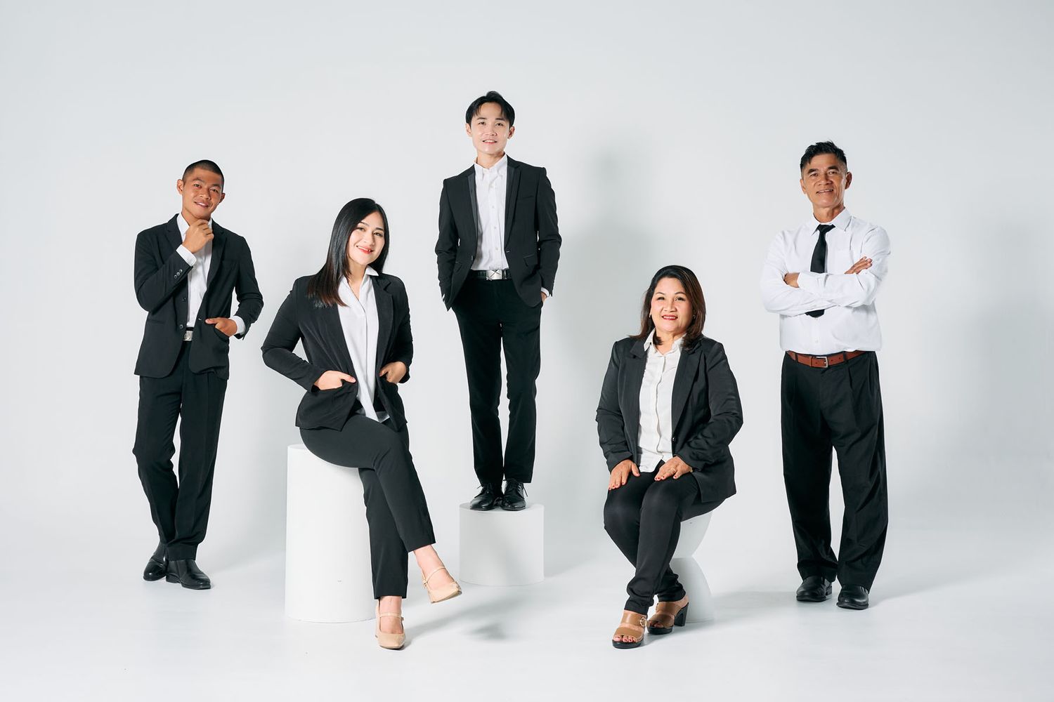 Five business professionals in black suits pose confidently against a white background in a corporate team photo.
