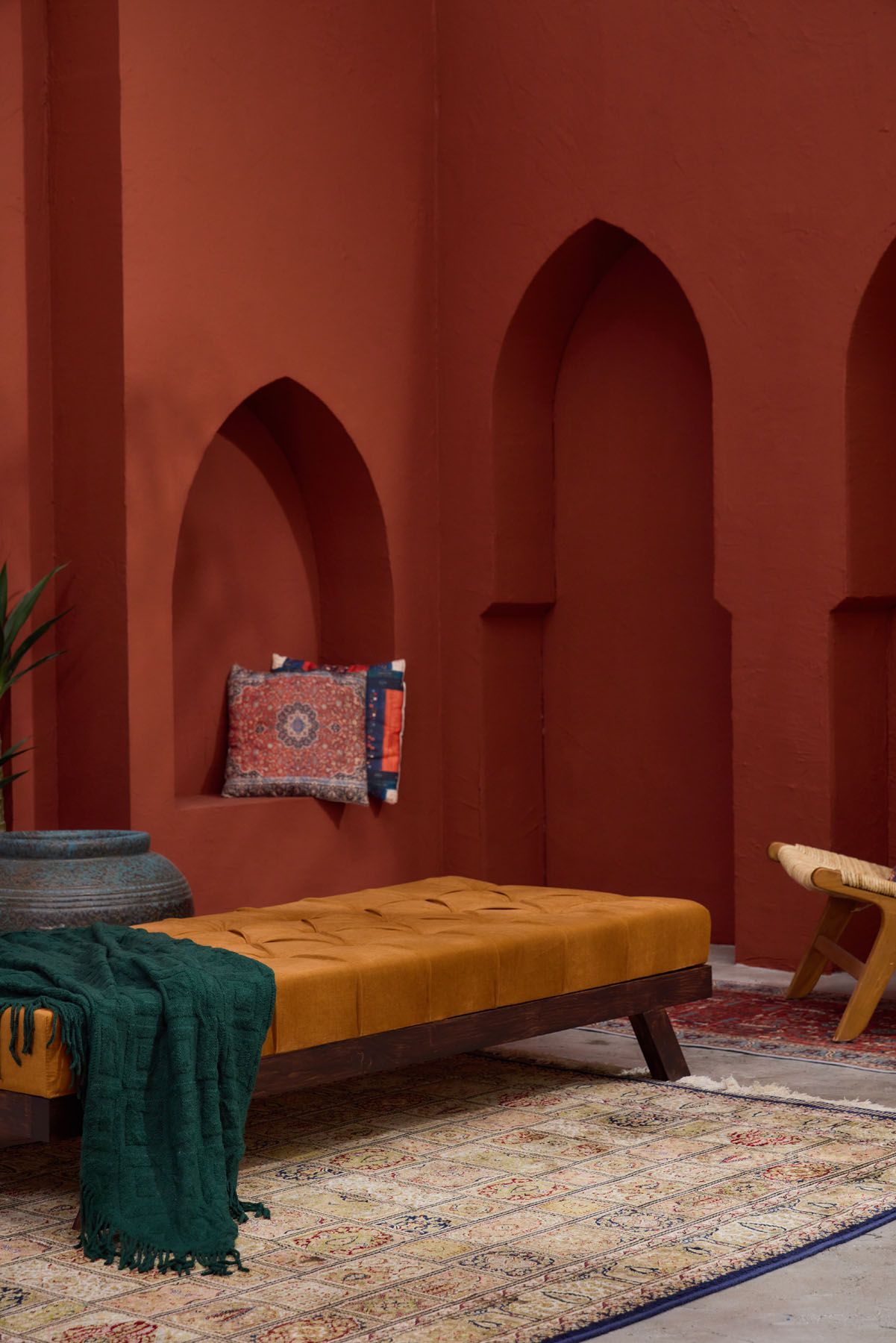 Moroccan riad interior with terracotta arched walls, mustard tufted daybed, emerald throw, and vintage patterned rug.
