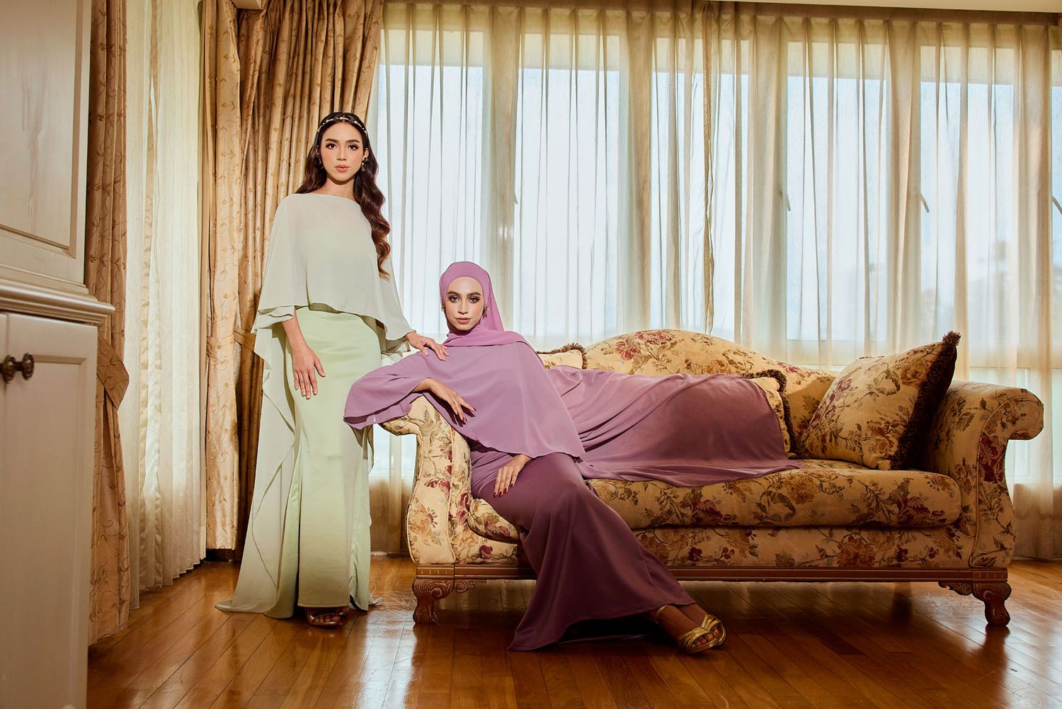 Two women in mint green and mauve purple modest fashion baju kurung in classic interior setting.