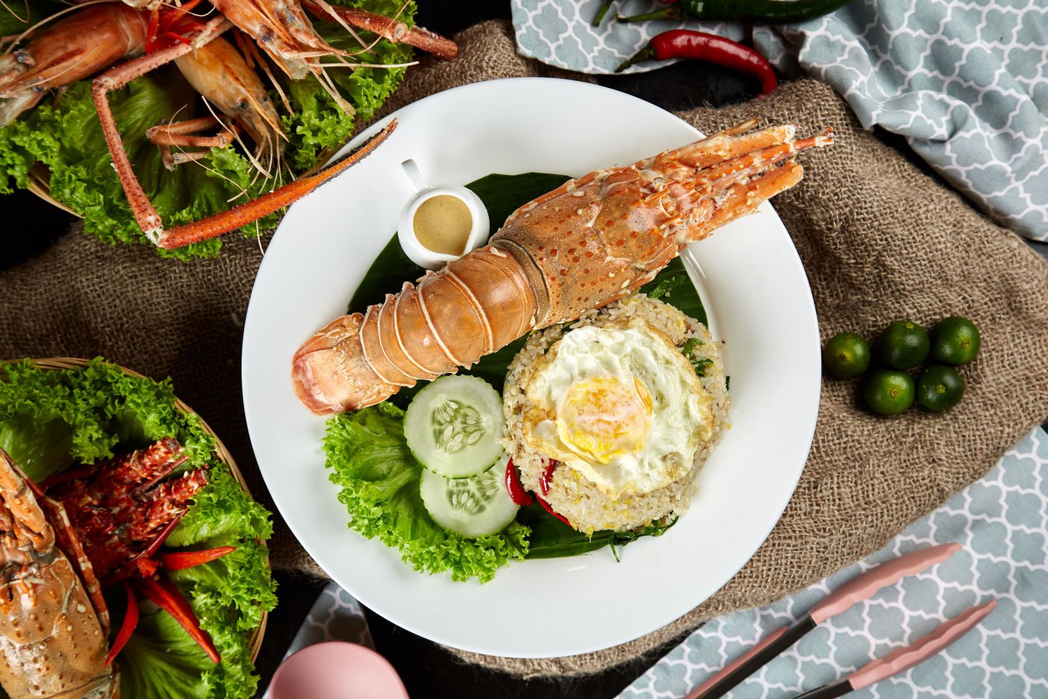 Overhead view of fried rice topped with egg and lobster tail garnished with fresh vegetables on white plate.