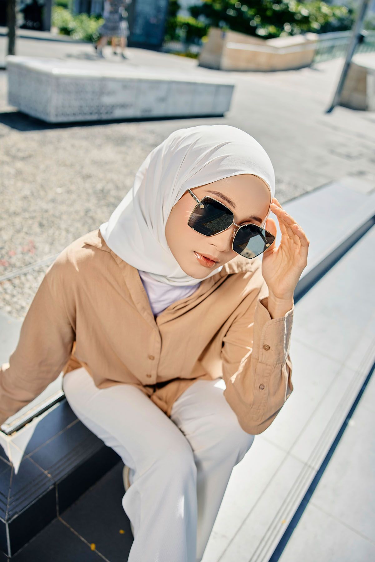 Stylish woman in white hijab and beige shirt wearing oversized sunglasses outdoors.