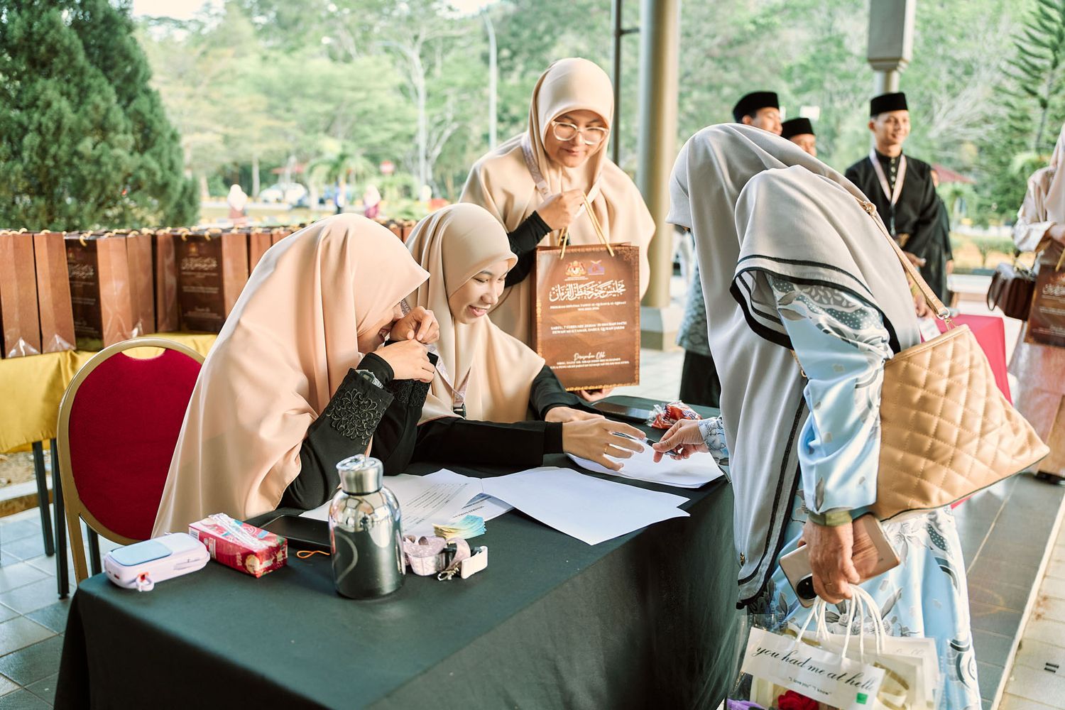 Women in hijab registering guests at welcome table during Malaysian Islamic event.