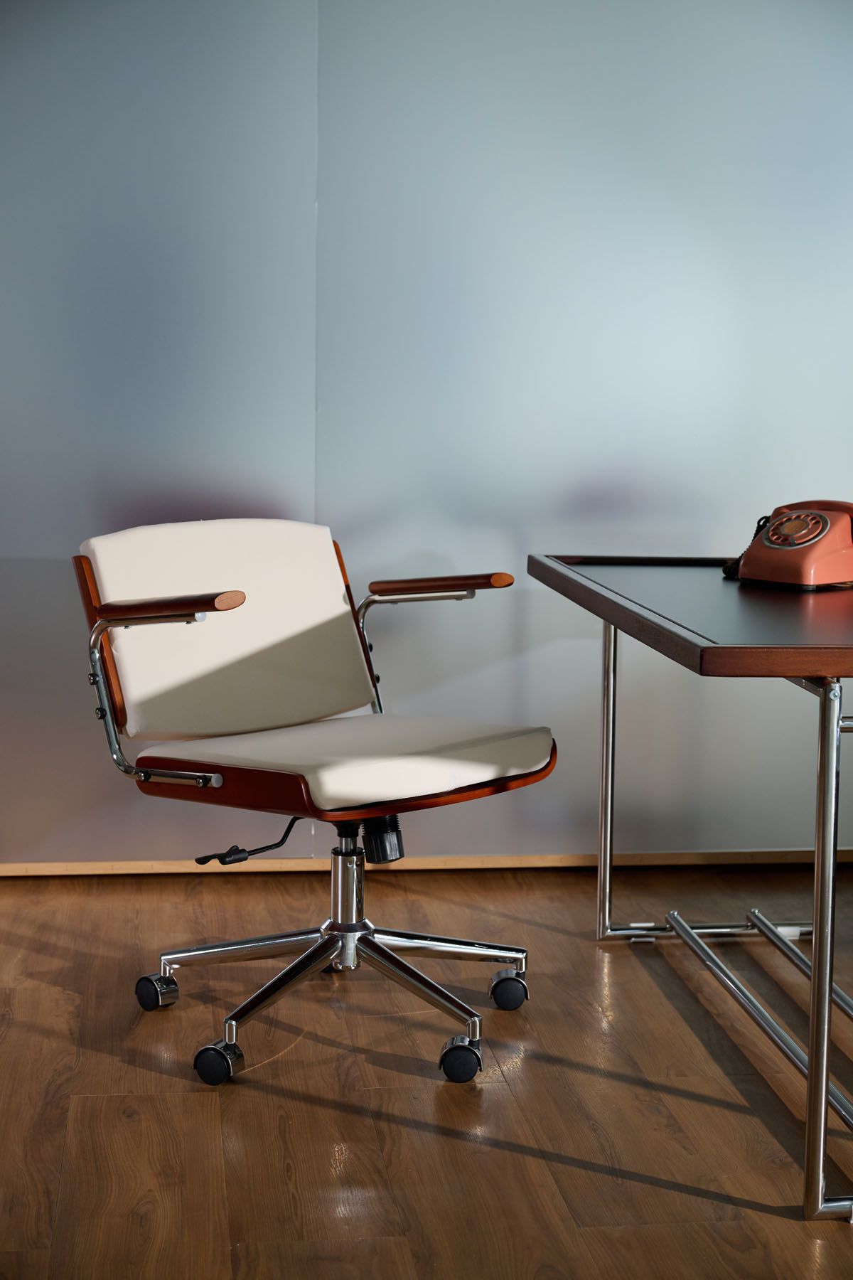 Retro office setup with a white leather swivel chair on casters beside a chrome desk with a vintage rotary phone.