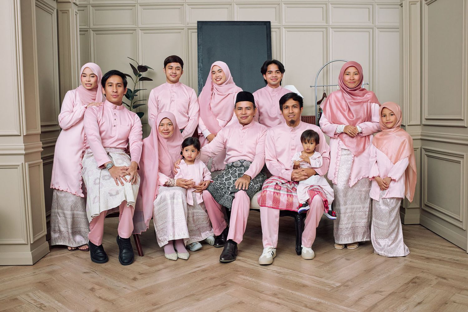 Muslim family in coordinated pink traditional Malay outfits posing for a formal Eid Raya celebration family photograph.
