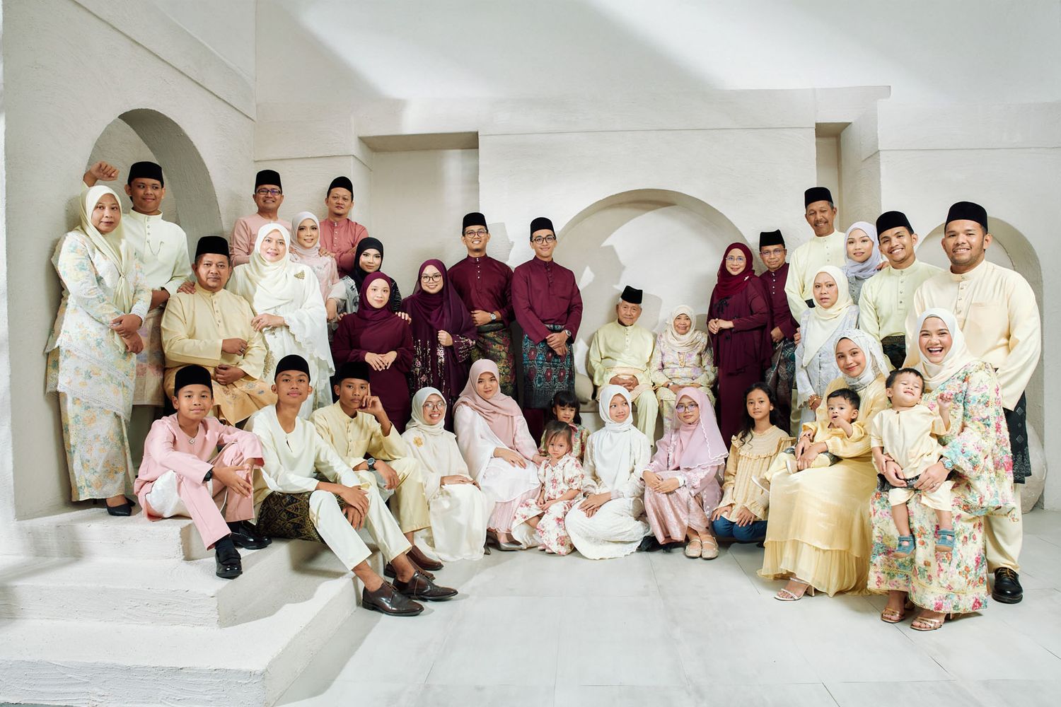 Large extended Malaysian family group photo in traditional Raya celebration outfits indoors.