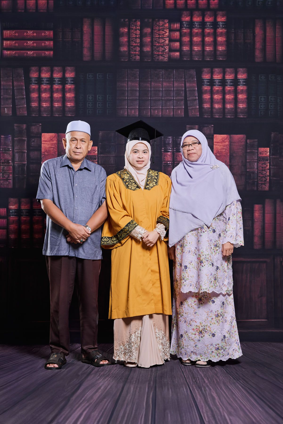 Muslim family celebrating graduation with daughter in golden robe and mortarboard cap indoors.
