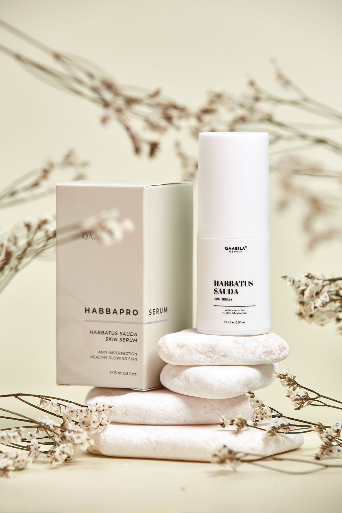 Qaabila Habbapro Habbatus Sauda skin serum pump bottle with beige box on white stones and dried flowers.