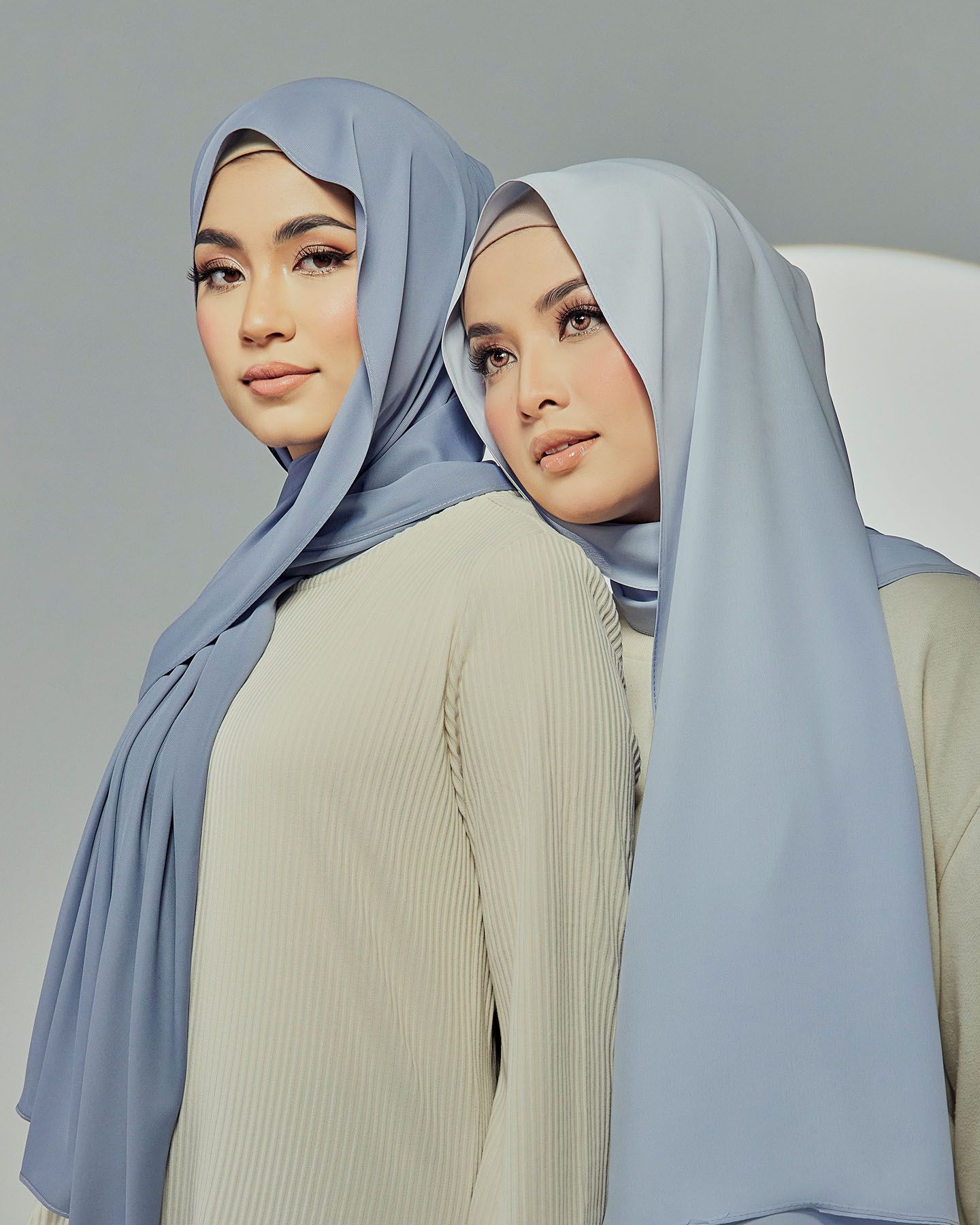 Two women wearing soft blue chiffon hijabs in a stylish fashion editorial pose.