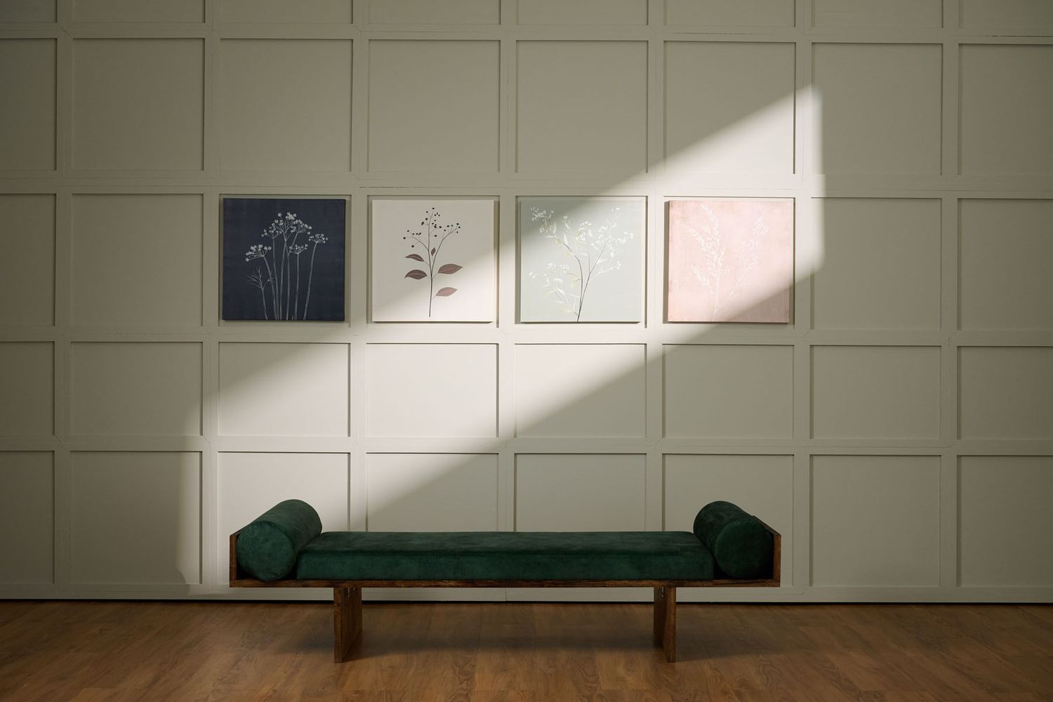 Green velvet bench against a sage wall with botanical art prints, bathed in natural light on hardwood floors.