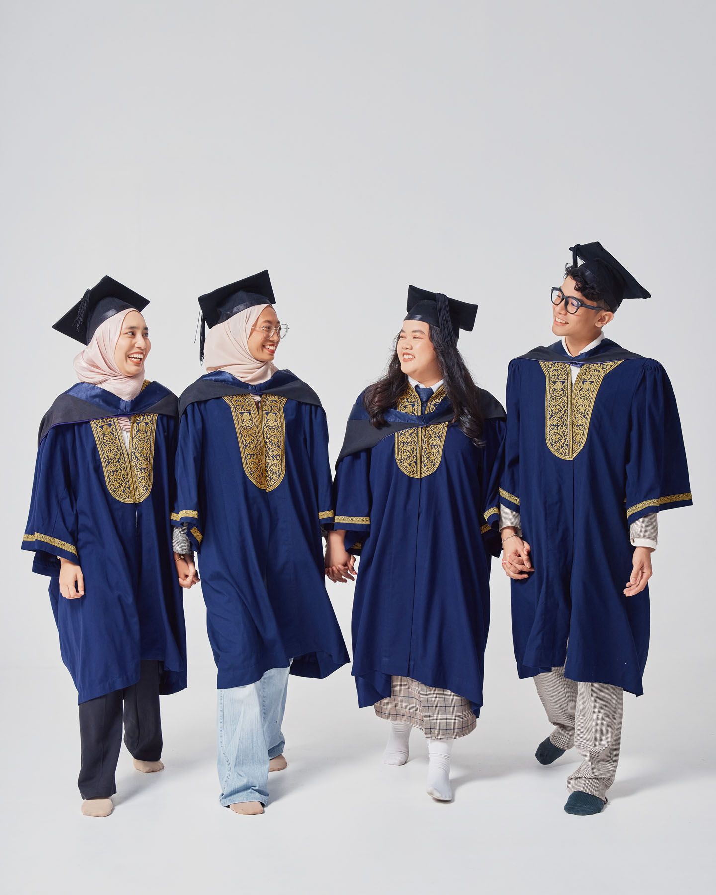 Four graduates in navy blue robes and mortarboards walking together smiling.