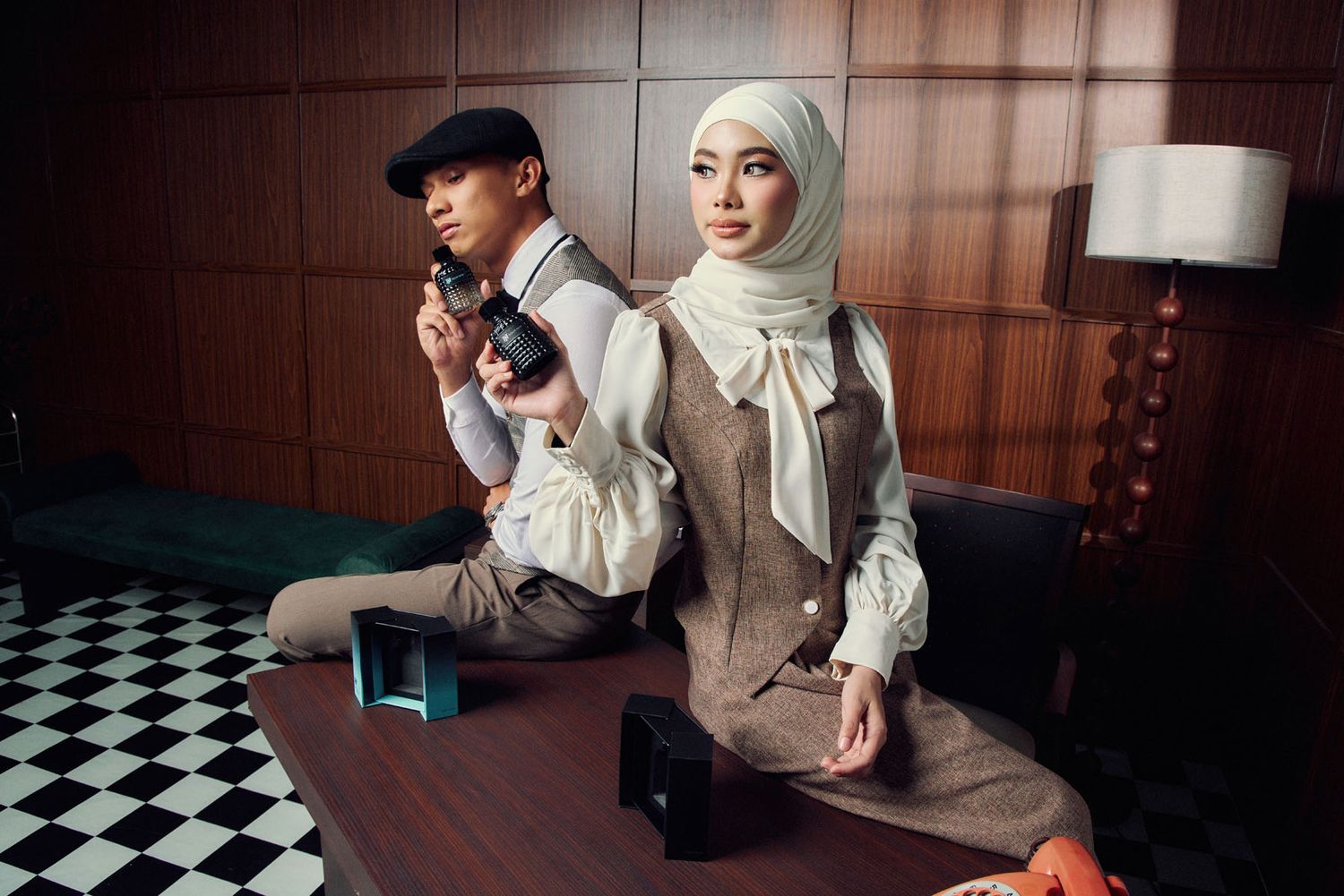Stylish couple in vintage-inspired outfits posing with a camera in a retro-decorated interior setting.