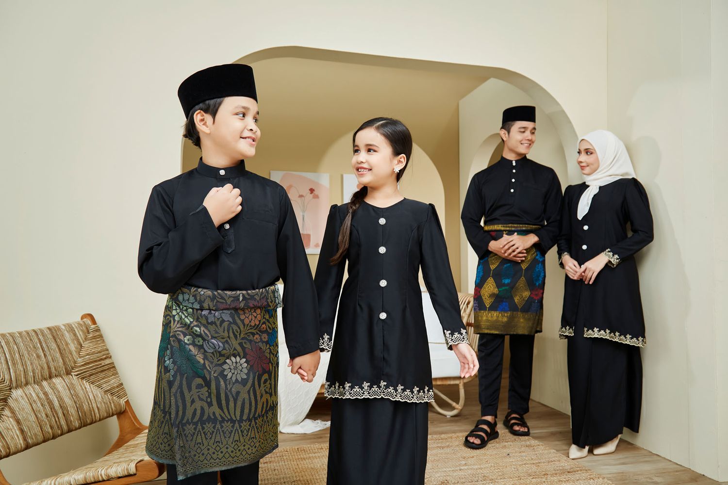 Children and adults in matching black traditional Malay outfits with batik details at home.