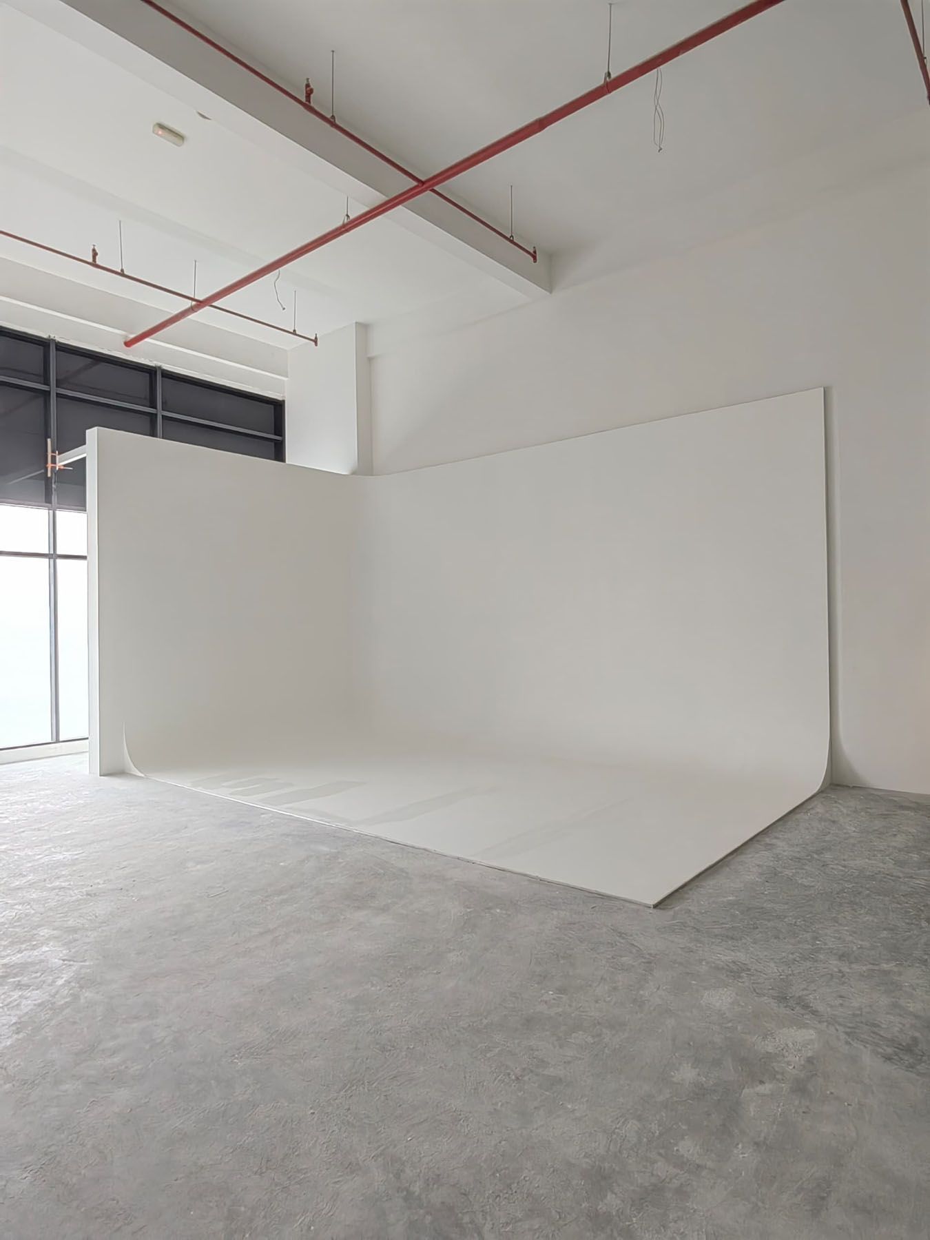 Spacious photography studio featuring a large white seamless backdrop with natural light from windows.
