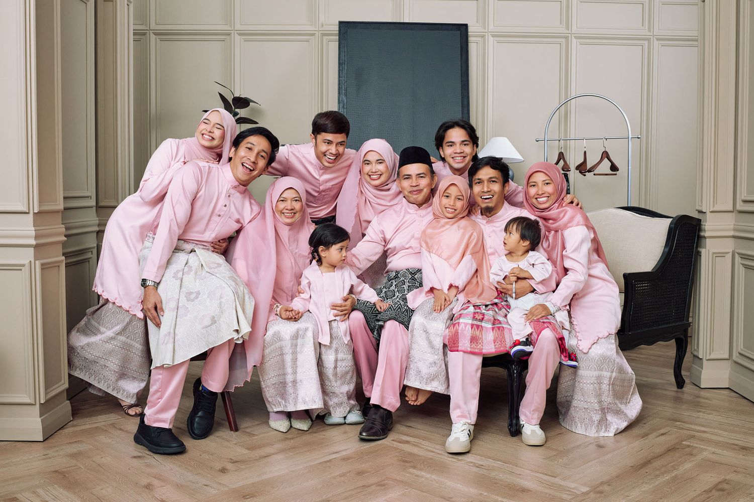 Large Muslim family in matching pink baju raya traditional outfits posing together for a festive Eid celebration photo.