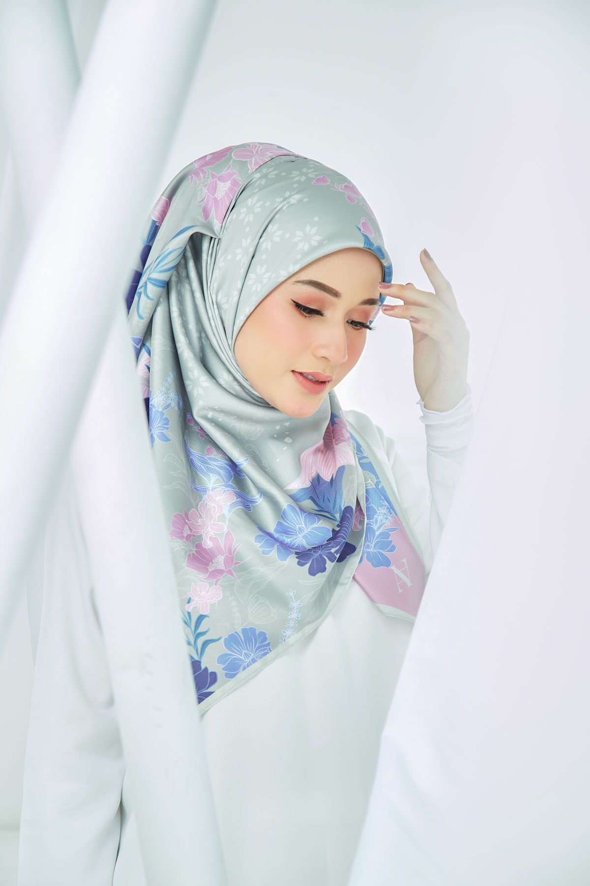 Woman wearing a light green floral printed hijab posing in a bright white studio setting.