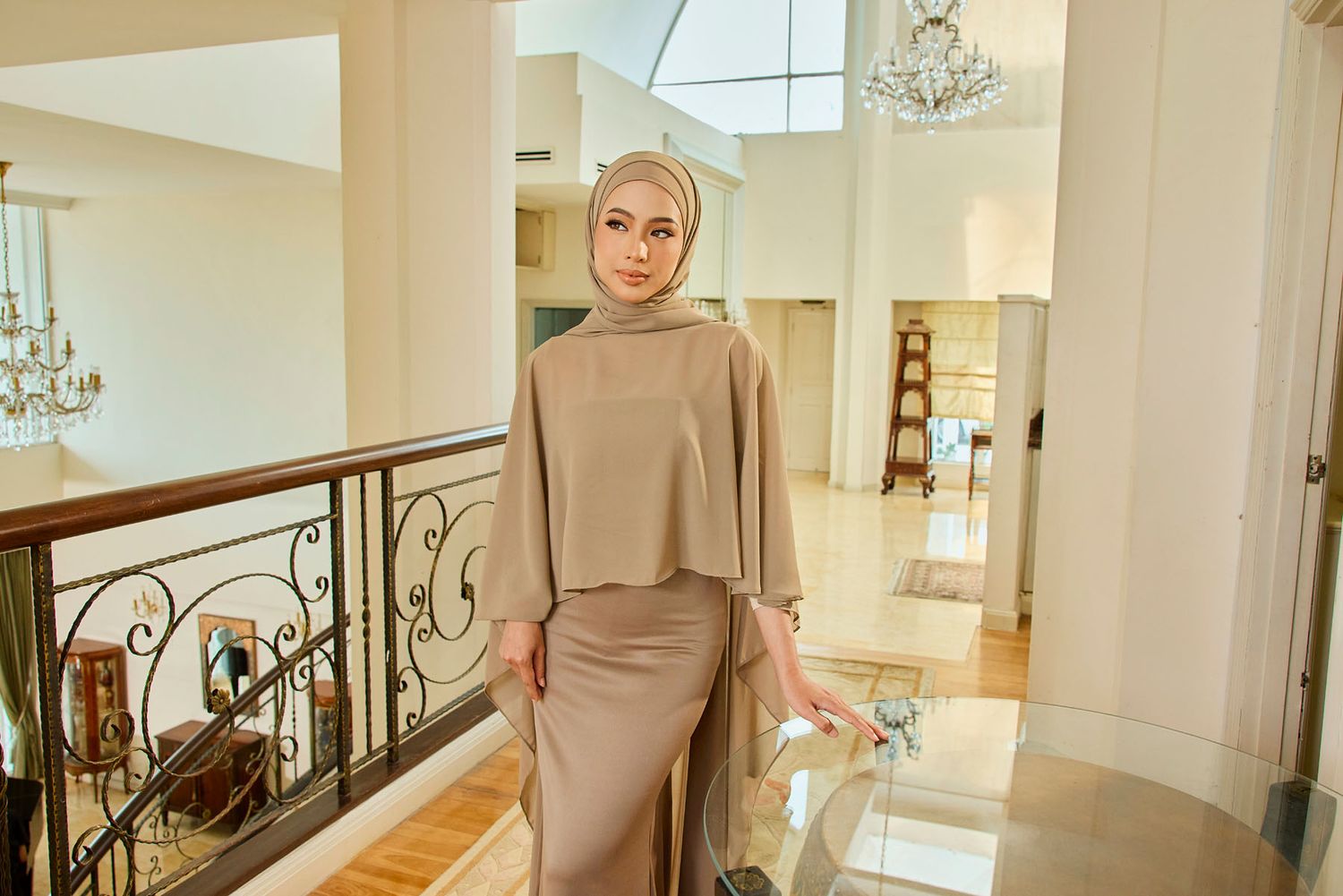 Woman in taupe hijab and matching modest outfit poses on elegant staircase in luxury interior.