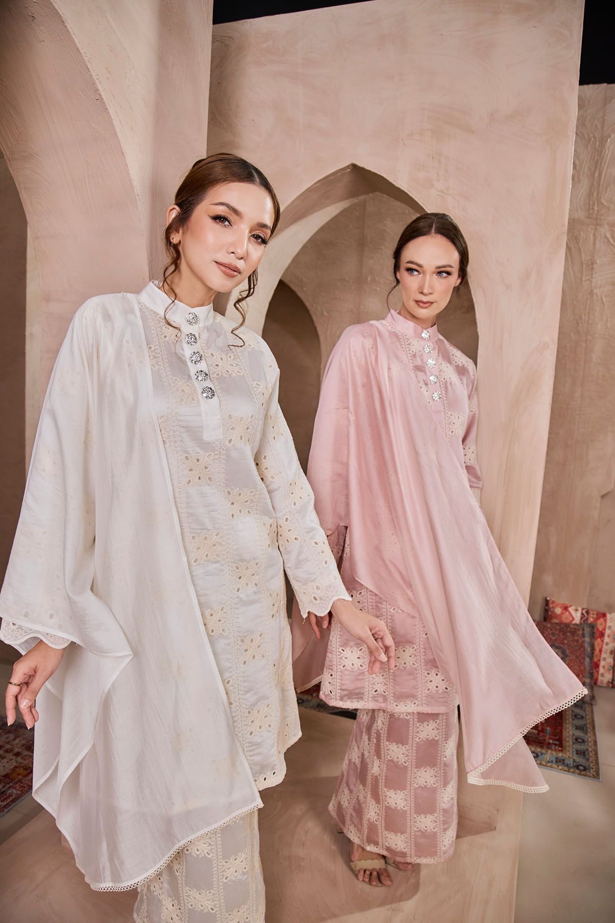 Two women in white and pink embroidered baju kurung with sheer overlay pose.