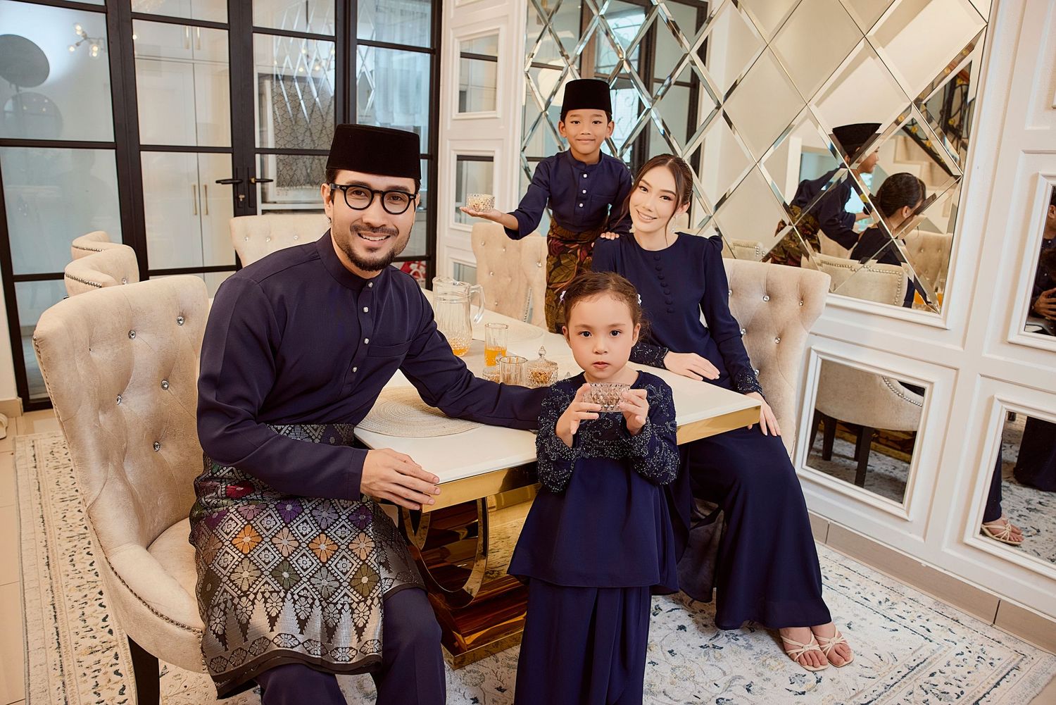 Family of four in matching navy blue traditional Malay baju kurung and baju melayu outfits pose together.