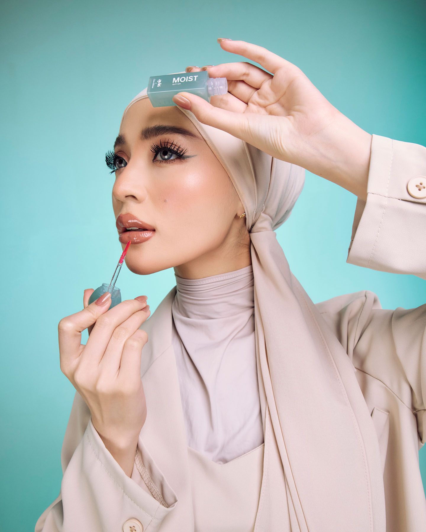 Muslim woman in hijab applying teal lip product while holding MOIST labeled item.