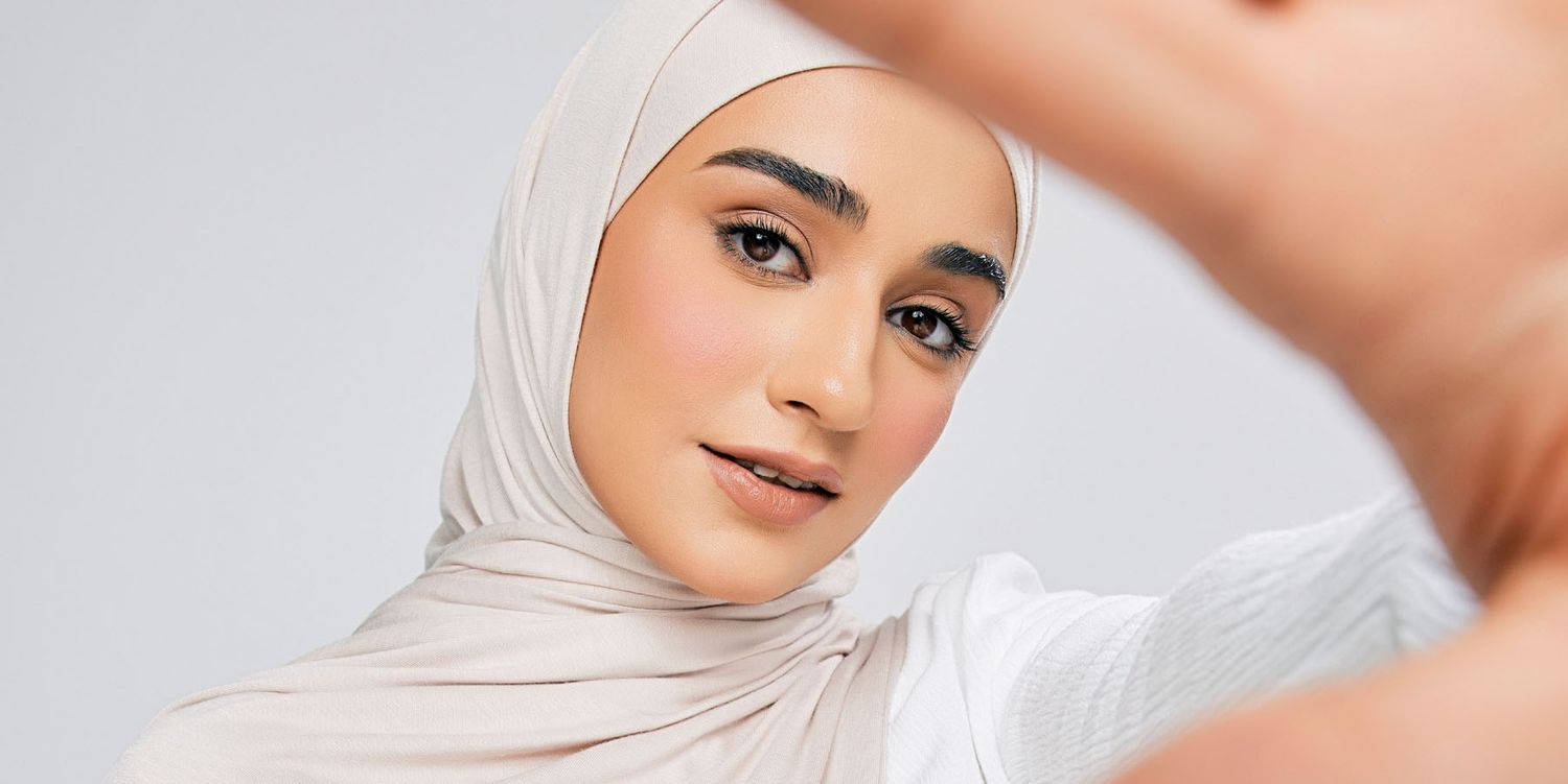 Close-up portrait of a young woman wearing a light beige hijab with natural makeup.