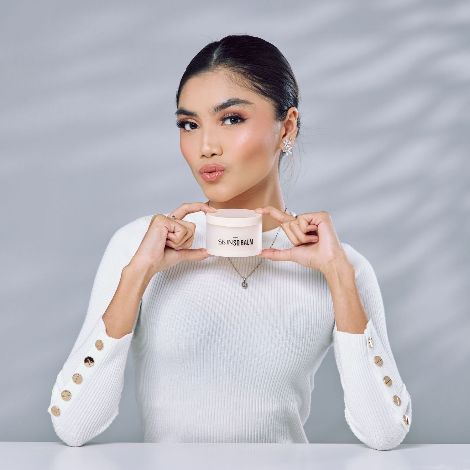 Woman in white ribbed top holding skincare cream jar product against light background.