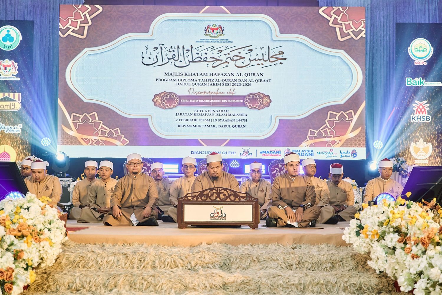 Group of men in traditional Islamic attire performing Quran recitation on a decorated stage at a formal Malaysian ceremony.