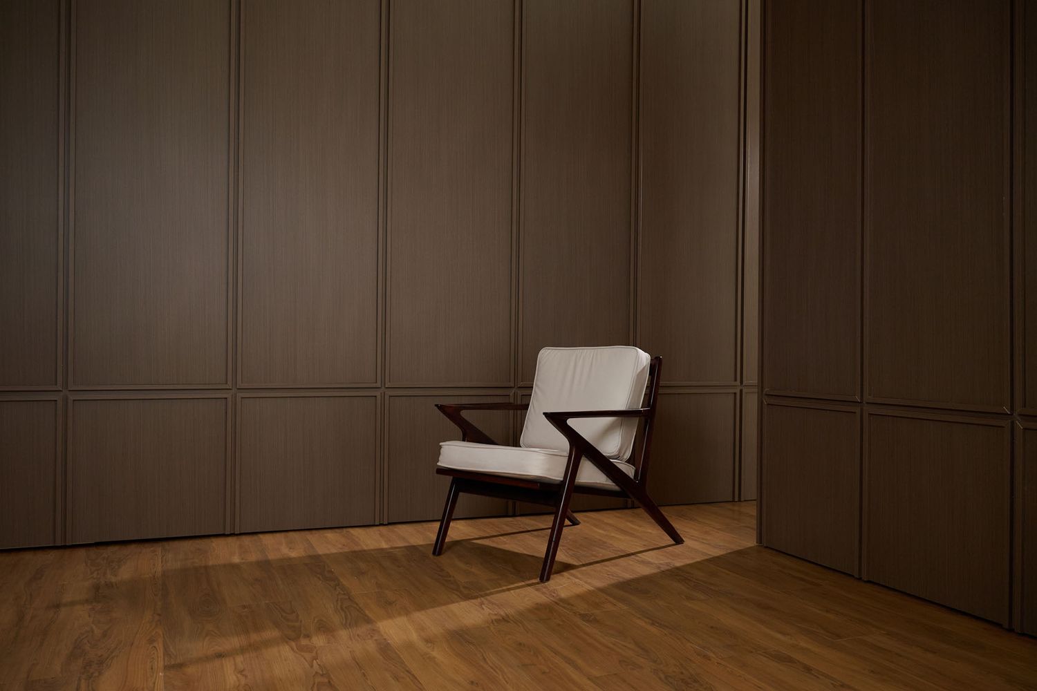 Mid-century modern armchair with light upholstery and dark wood frame in a minimalist room with wood floors.